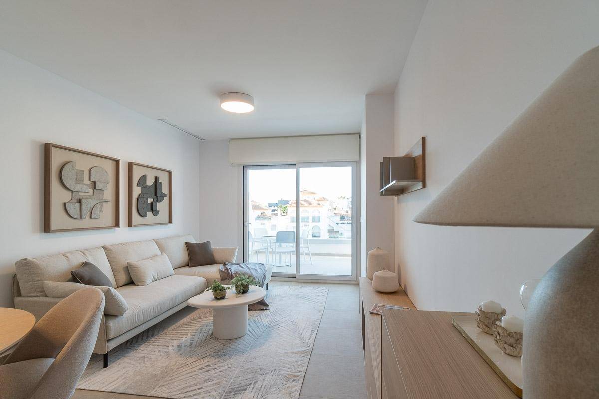 Helles Wohnzimmer mit beigem Sofa, Couchtisch und Zugang zu einem Balkon mit Blick auf die Umgebung.