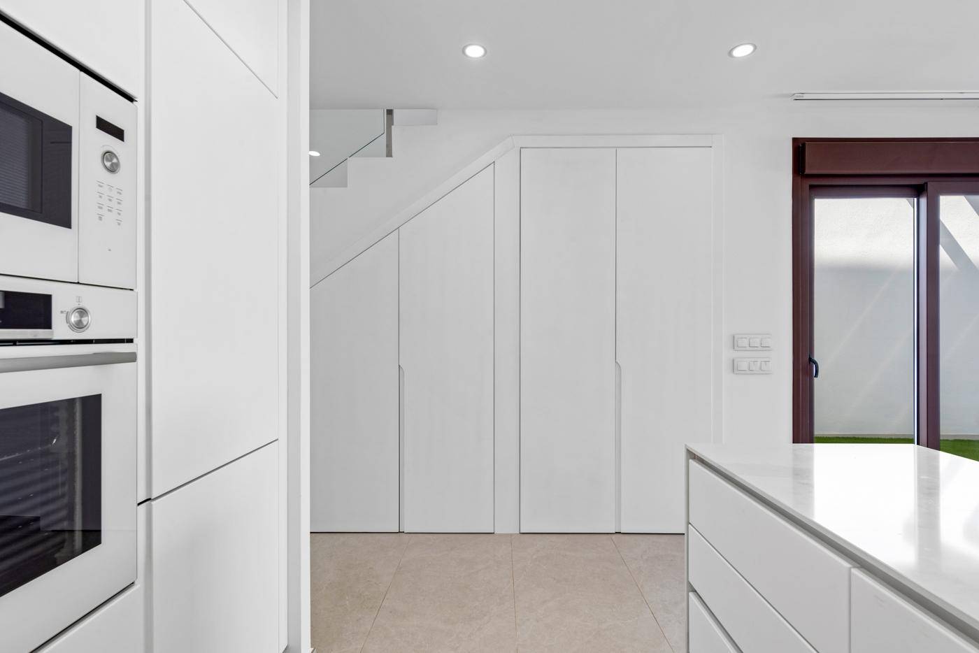 Moderne weiße Küche mit Einbaugeräten und integrierten Schränken unter der Treppe.