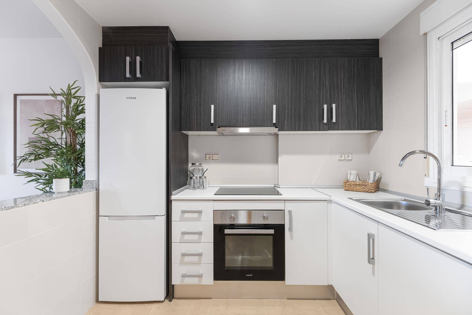 Funktionale Küche mit weißen und dunklen Schränken, Kühlschrank und Kochfeld.