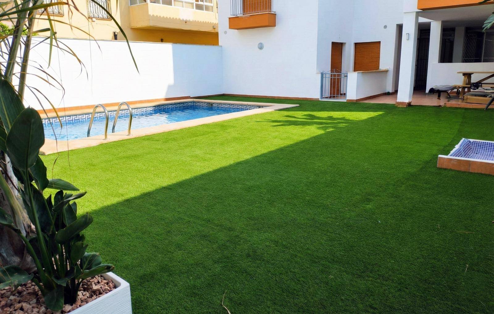Großer Gartenbereich mit Kunstrasen, einem kleinen Pool und hohen Mauern für Privatsphäre.
