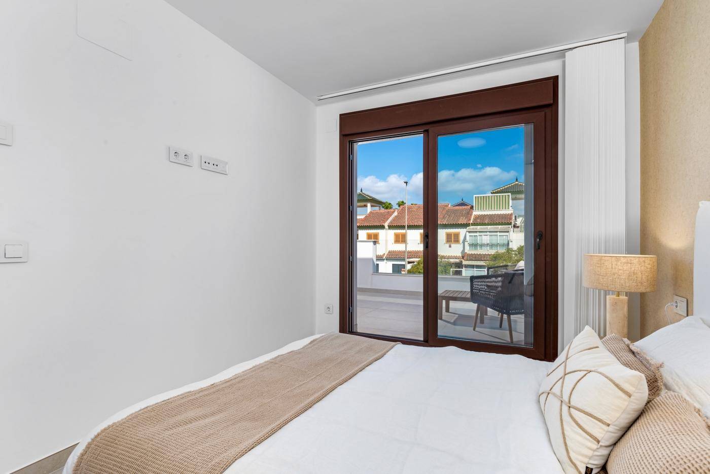 Schlafzimmer mit großem Fenster und Zugang zum Balkon, mit Blick auf die Nachbarschaft.