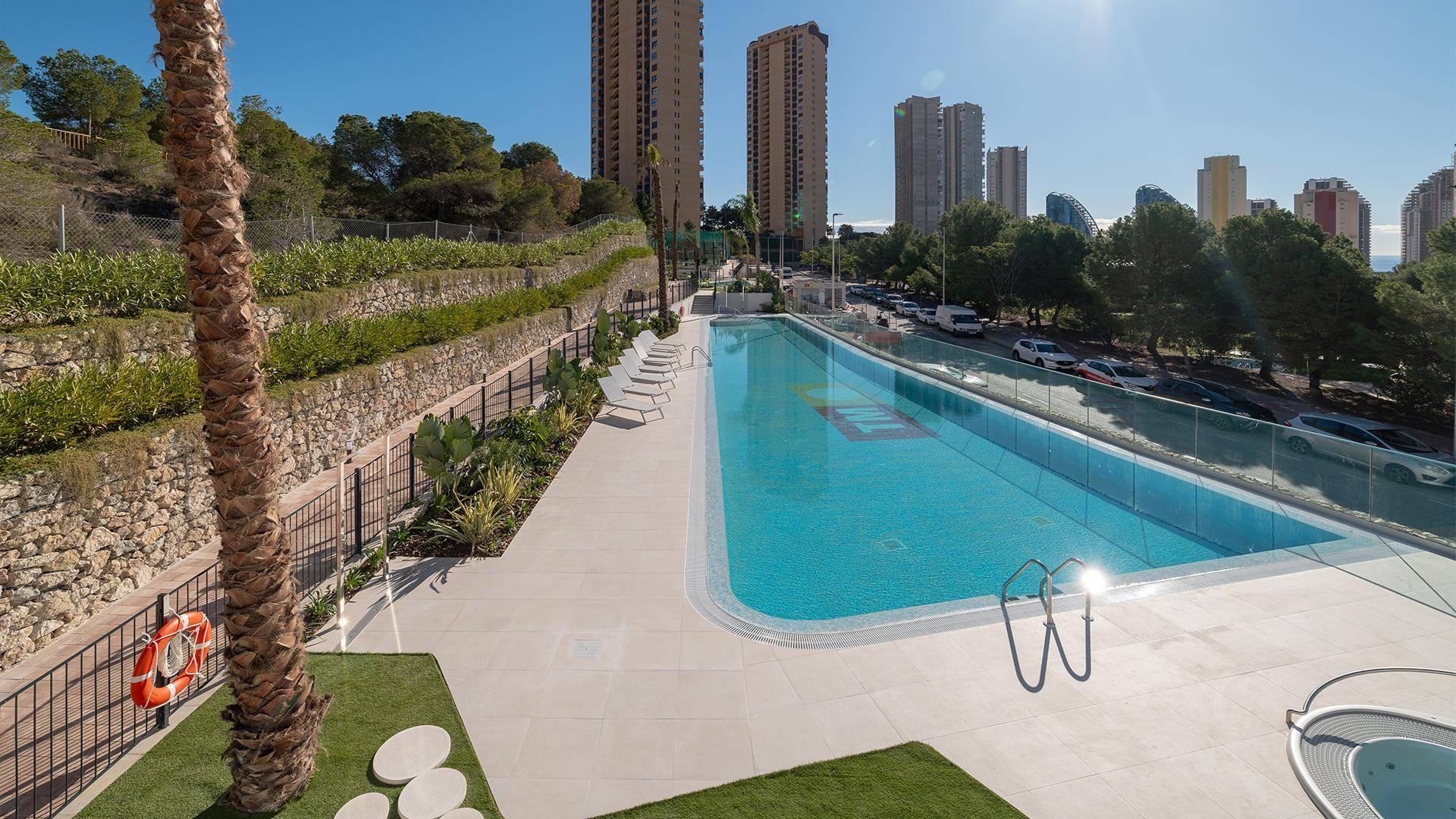 Großer Außenpoolbereich mit Liegestühlen und Blick auf die Stadt und das Meer.