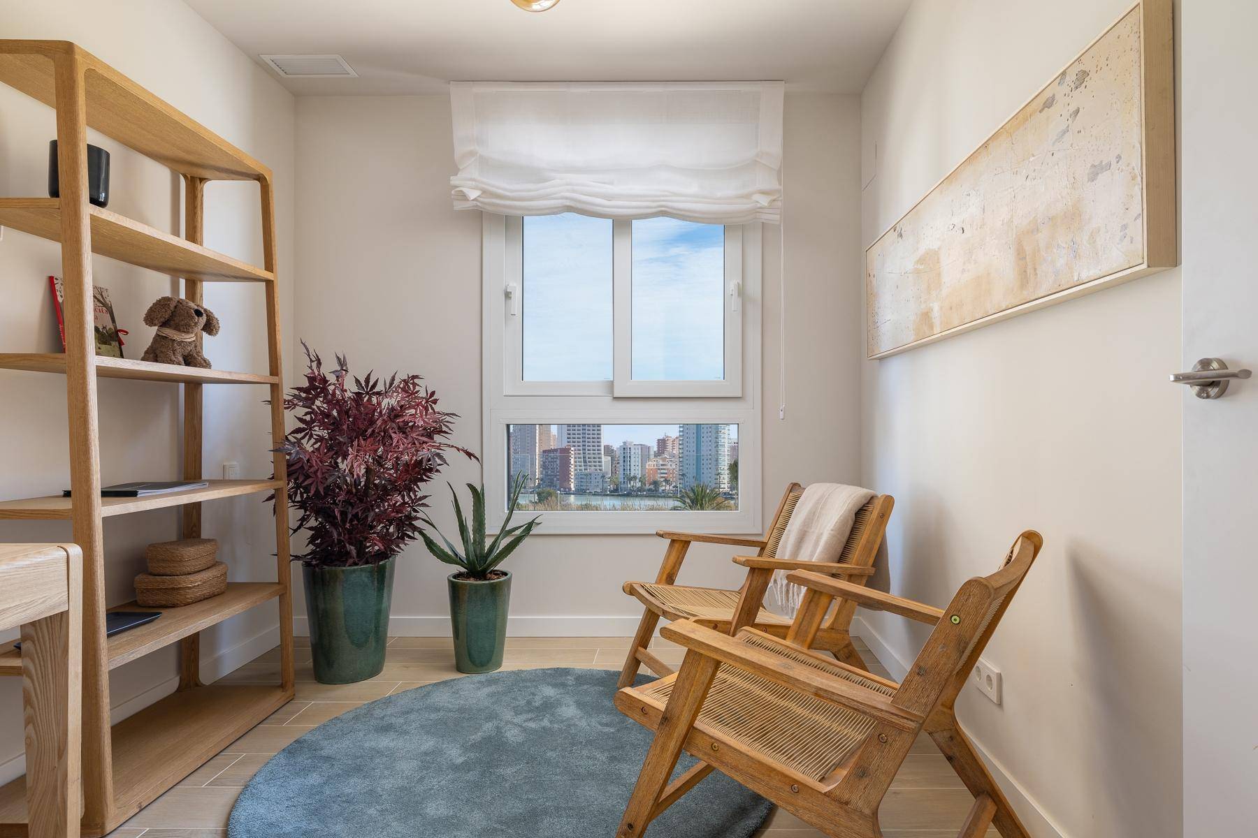 Helles Arbeitszimmer mit Fenster, zwei Holzstühlen, einem Bücherregal und Zimmerpflanzen.