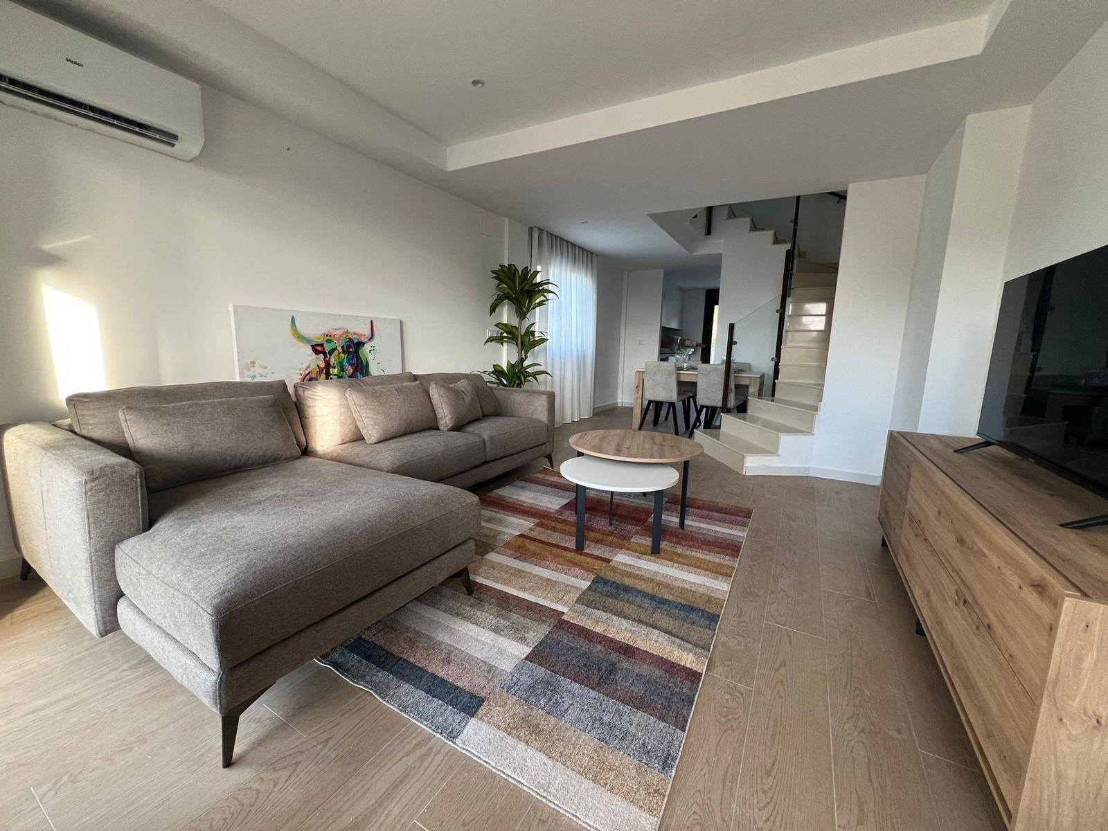 Offener Wohn- und Essbereich mit modernem Sofa, Teppich und Treppe zum Obergeschoss.