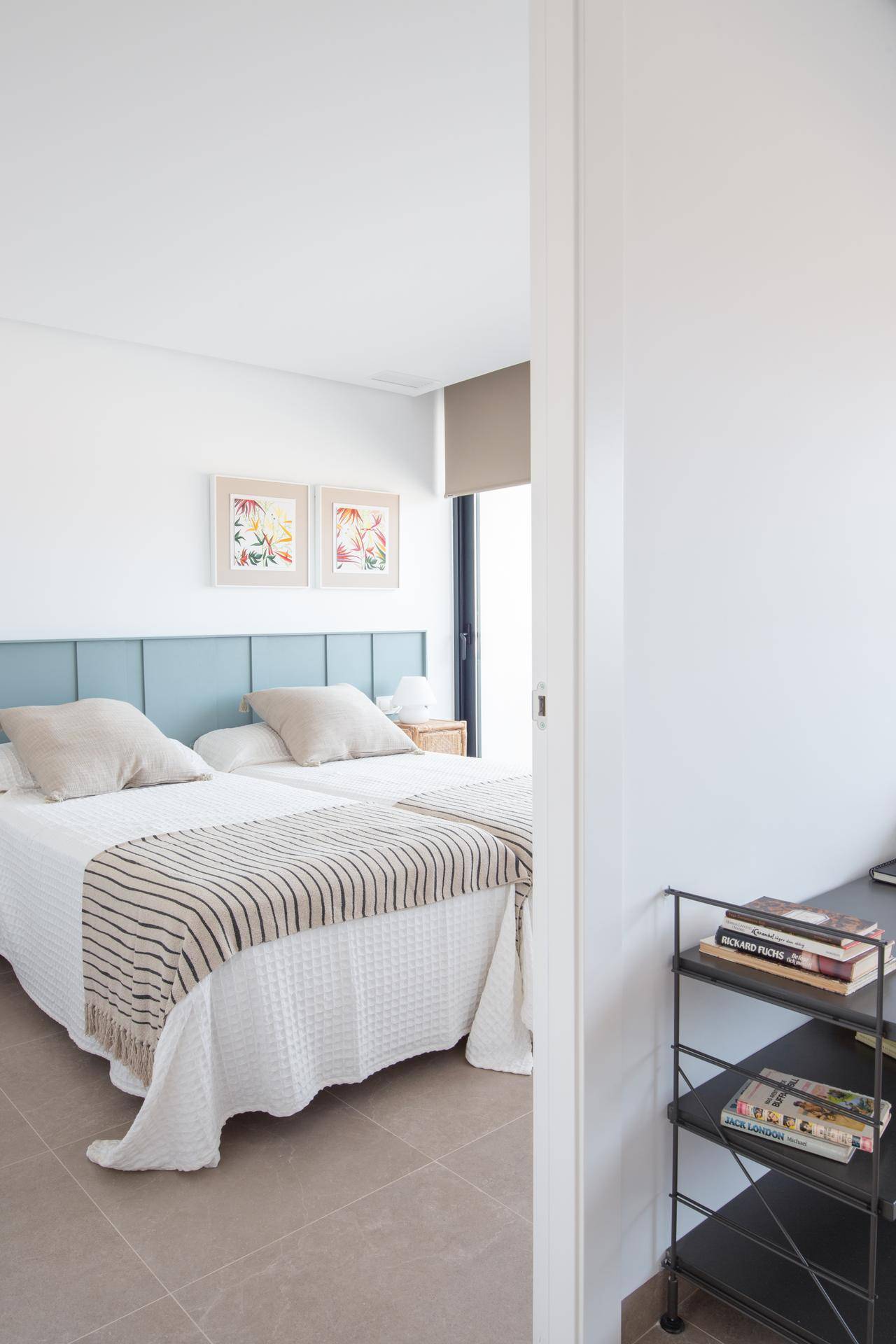 Schlafzimmer mit zwei Einzelbetten, gepolstertem Kopfteil und Fenster mit modernem Rollo.