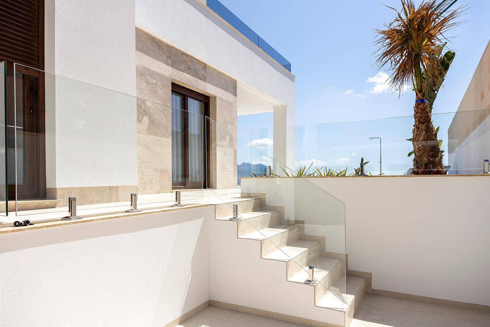Moderne Außentreppe mit Glasgeländer, die zu einem oberen Bereich der Villa führt.