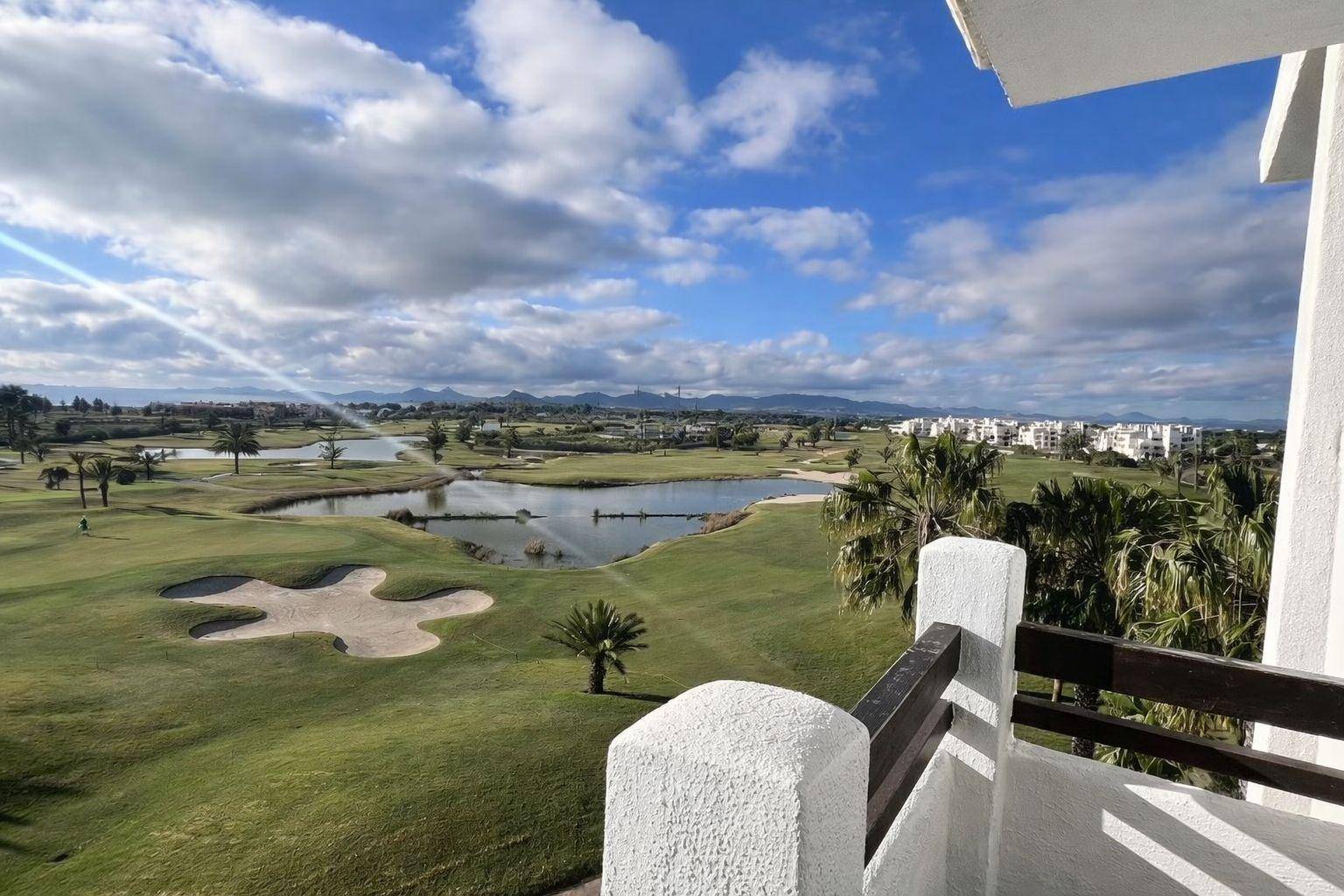 Panoramablick von einem Balkon auf einen weitläufigen Golfplatz mit Seen und Bergen im Hintergrund.