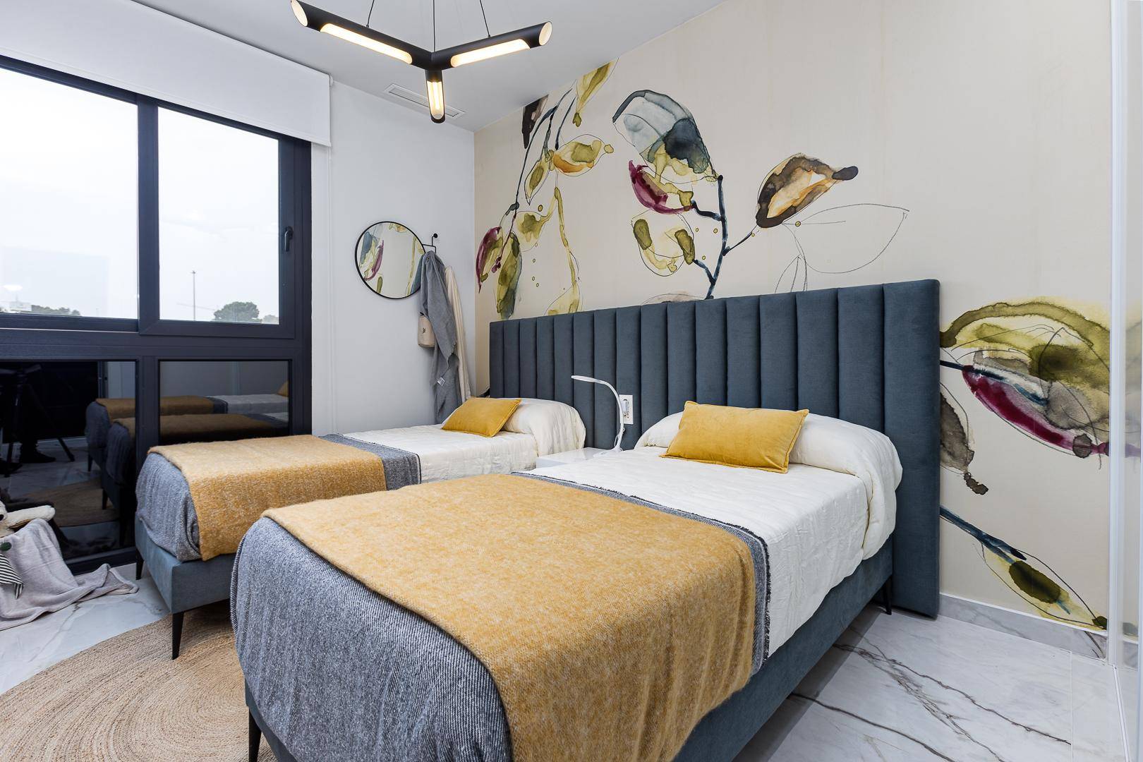 Helles Schlafzimmer mit zwei Einzelbetten, farbenfroher Tapete und großem Fenster.