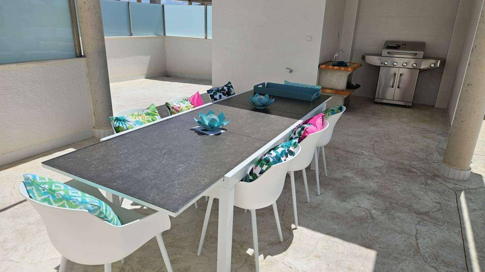 Moderner Esstisch mit bunten Kissen auf der Dachterrasse, ideal für Mahlzeiten im Freien.