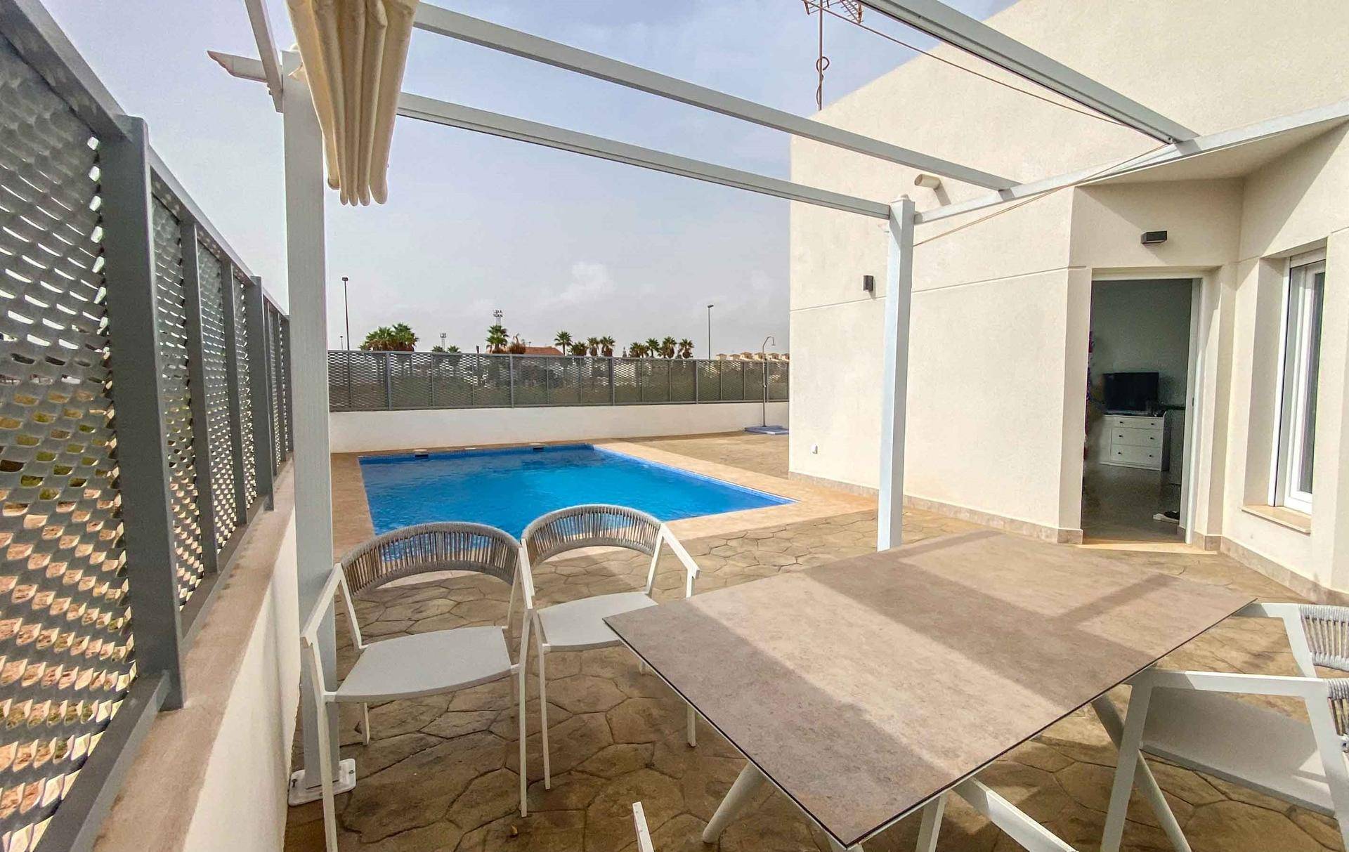 Geräumige Terrasse mit Esstisch, Pergola und Blick auf den Poolbereich.