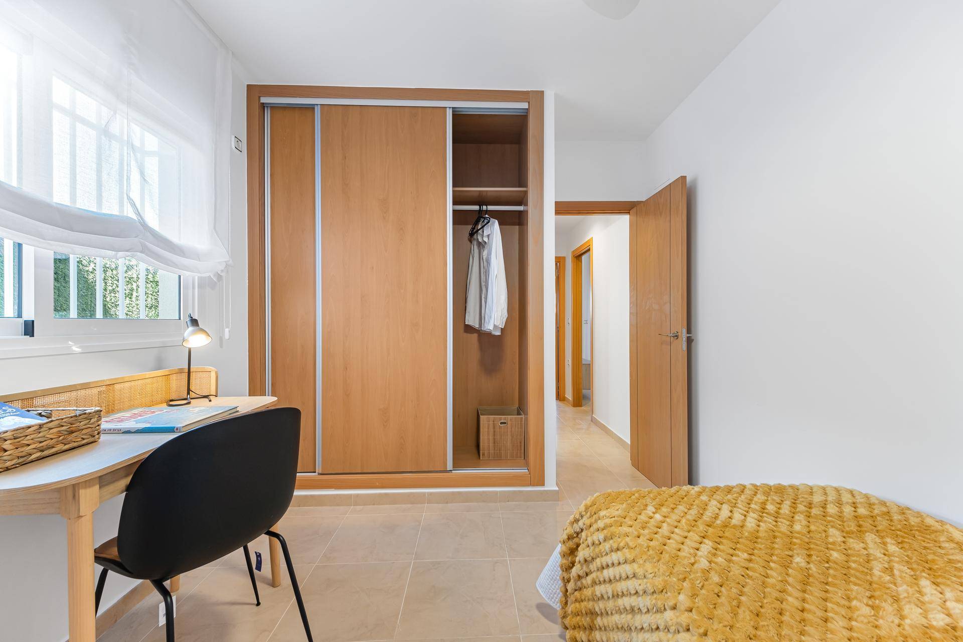 Einzelzimmer mit integriertem Holzschrank, Schreibtisch und Zugang zum Flur.