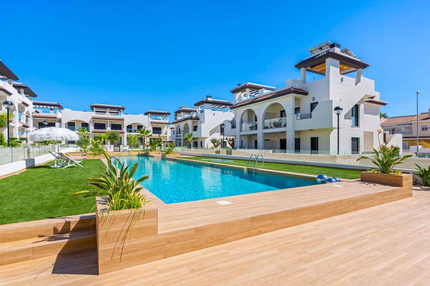 Weitläufige Poolanlage mit Holzdeck und grünen Rasenflächen, umgeben von modernen Wohngebäuden.