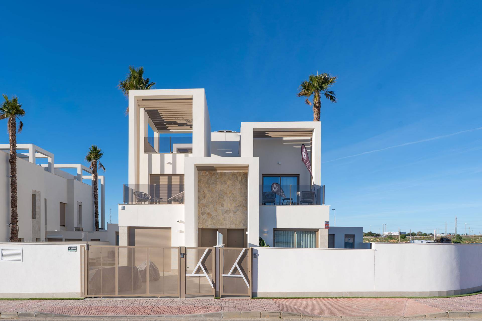 Moderne weiße Villa mit klaren Linien, Balkonen und Palmen unter strahlend blauem Himmel.