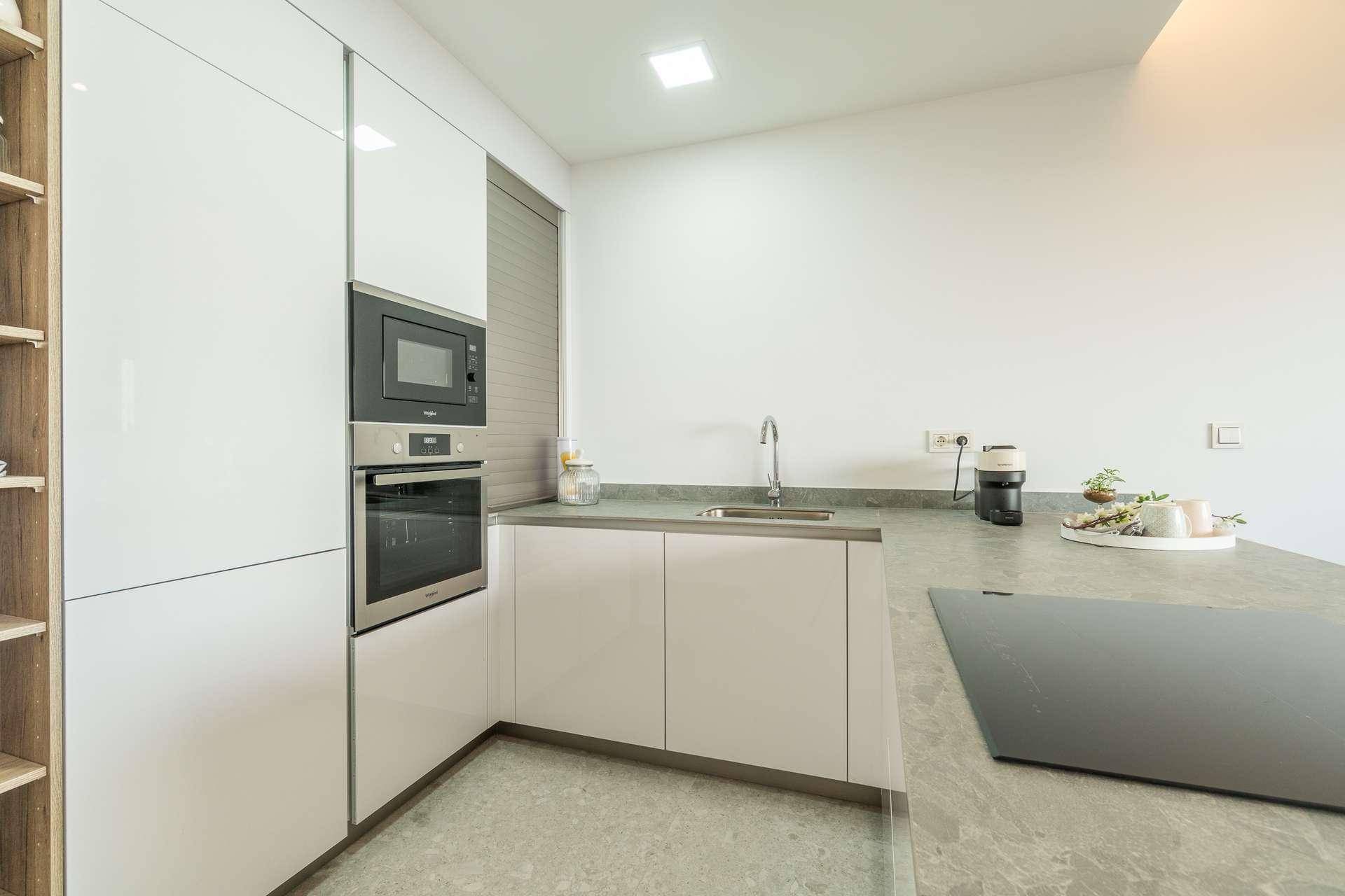 Moderne Küche mit weißen Hochglanzschränken, integriertem Backofen und Mikrowelle.