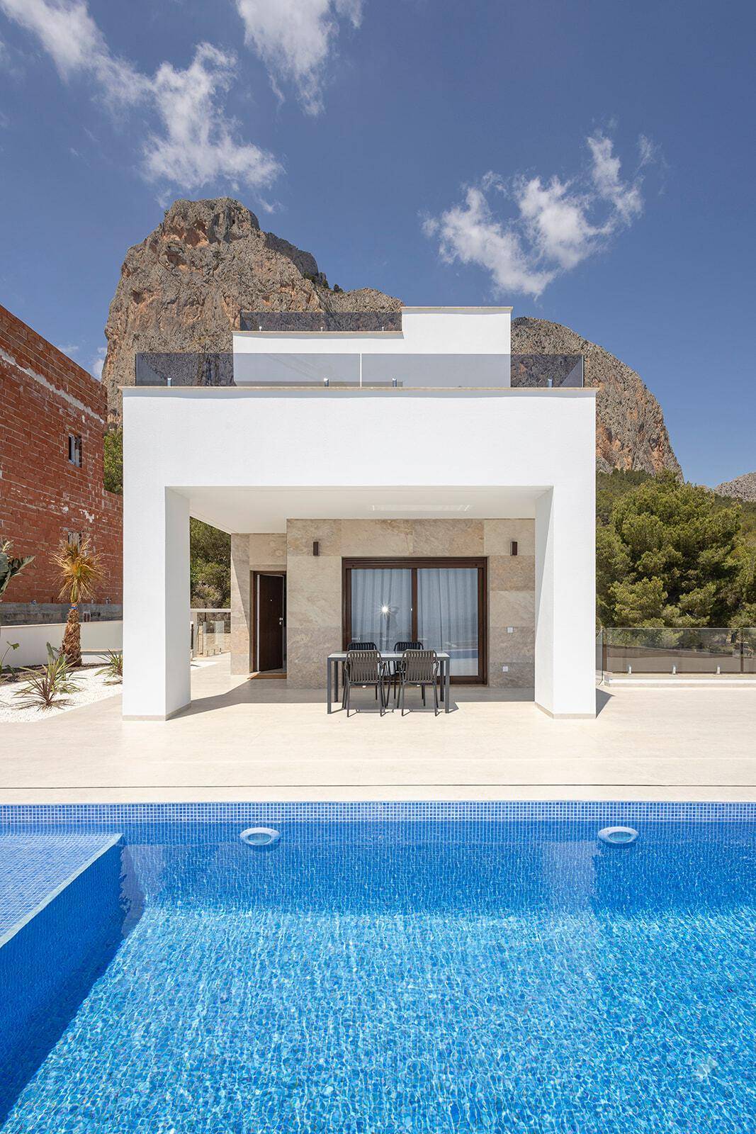 Blick auf die moderne Villa mit Pool und überdachtem Essbereich vor imposanter Bergkulisse.