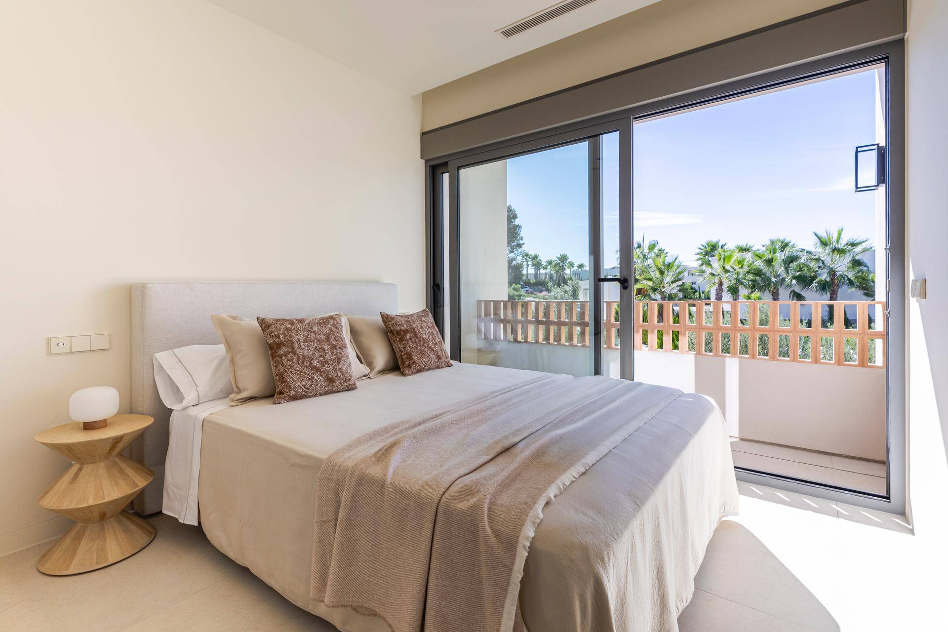 Helles Schlafzimmer mit Zugang zu einem Balkon und Blick auf die Palmen.
