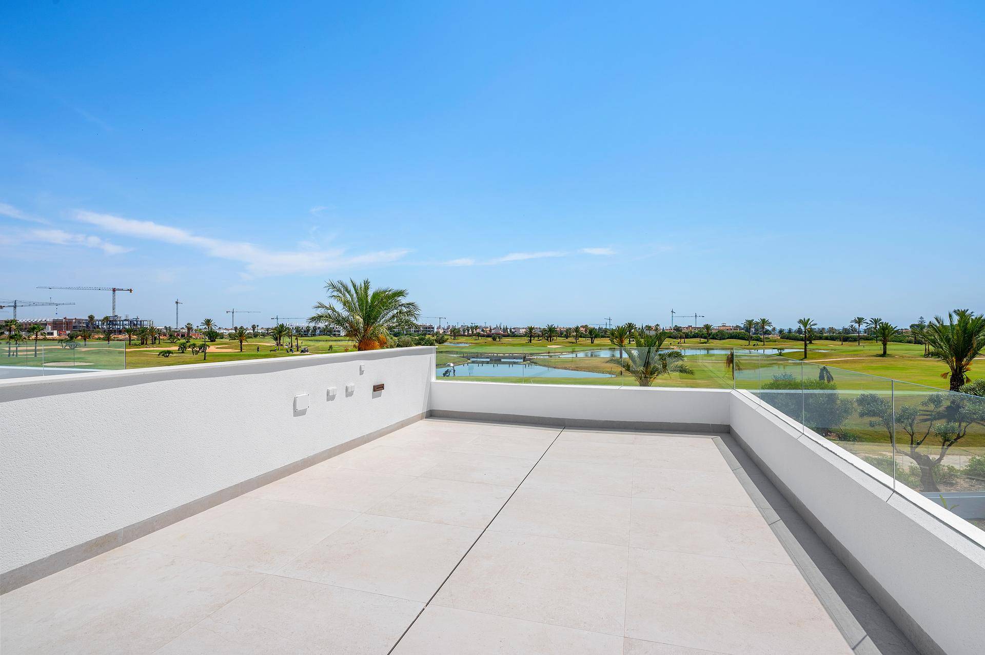 Geräumige Dachterrasse mit Fliesenboden und Glasgeländer, bietet einen weiten Blick auf den Golfplatz.