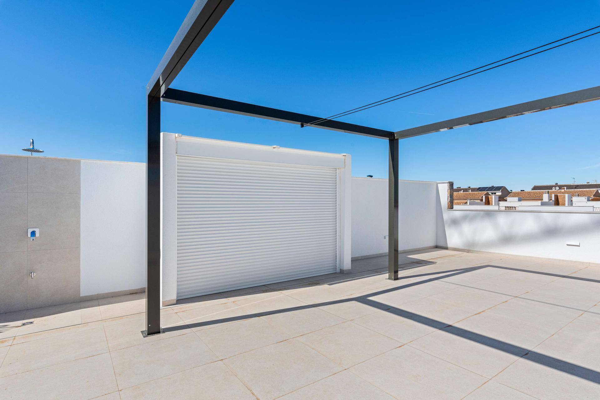 Dachterrasse mit Rollladenbereich und moderner Pergola unter strahlend blauem Himmel.