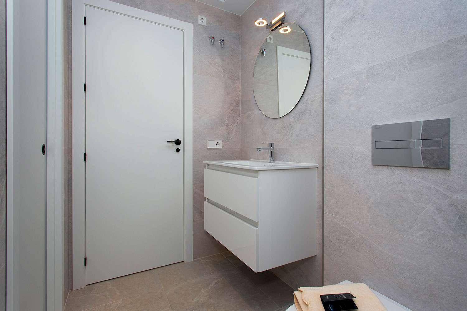 Modernes Badezimmer mit schwebendem Waschtisch, rundem Spiegel und Wand-WC, sehr funktional.
