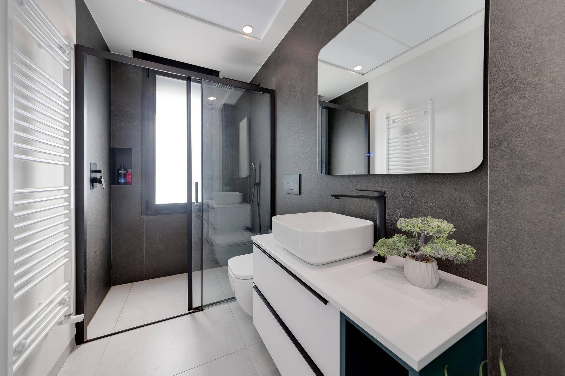 Modernes Badezimmer mit dunklen Fliesen, begehbarer Dusche und stilvollem Waschtisch mit Fenster.