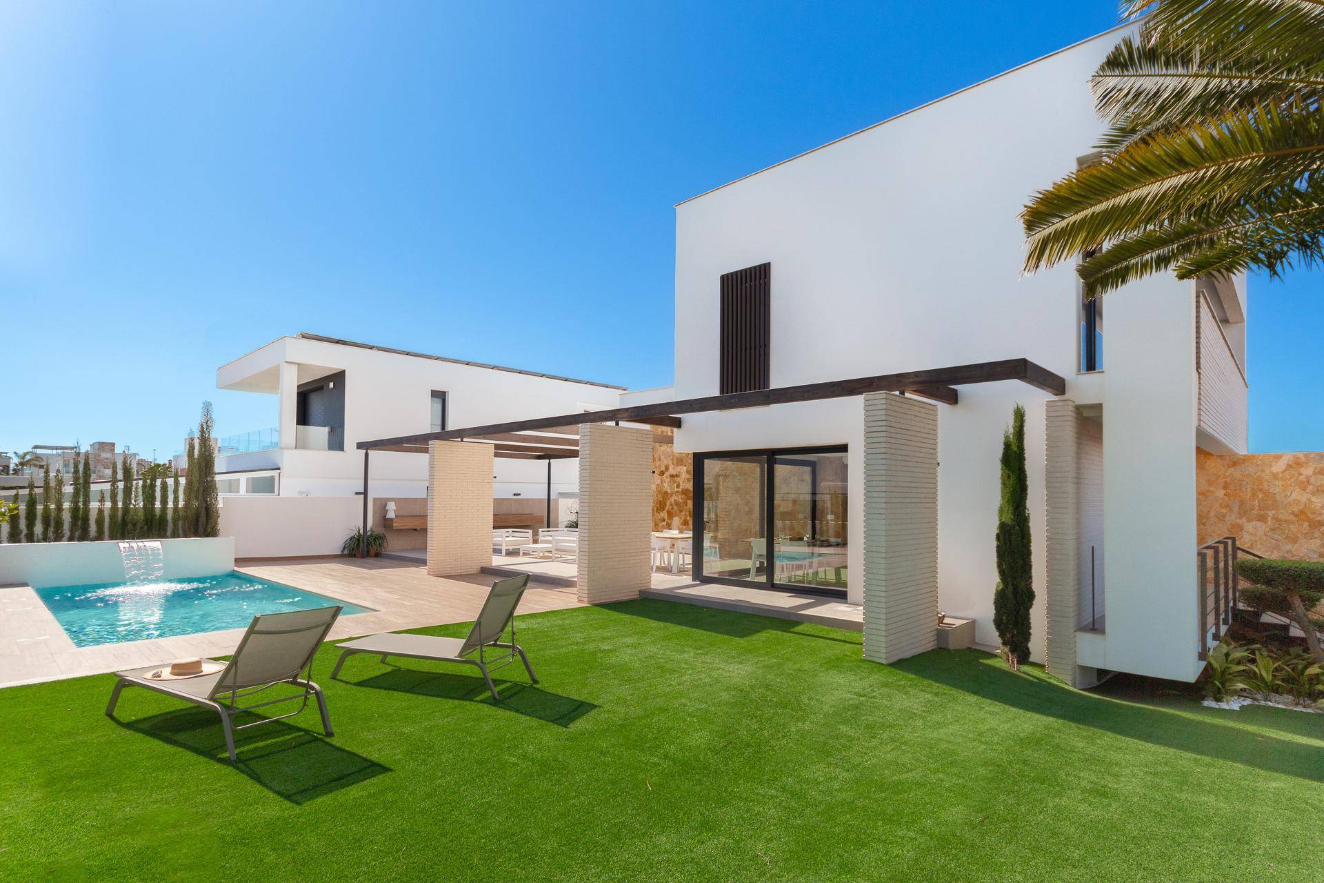 Seitlicher Blick auf die moderne Villa mit Pool, Kunstrasen und weiteren Gebäuden im Hintergrund.