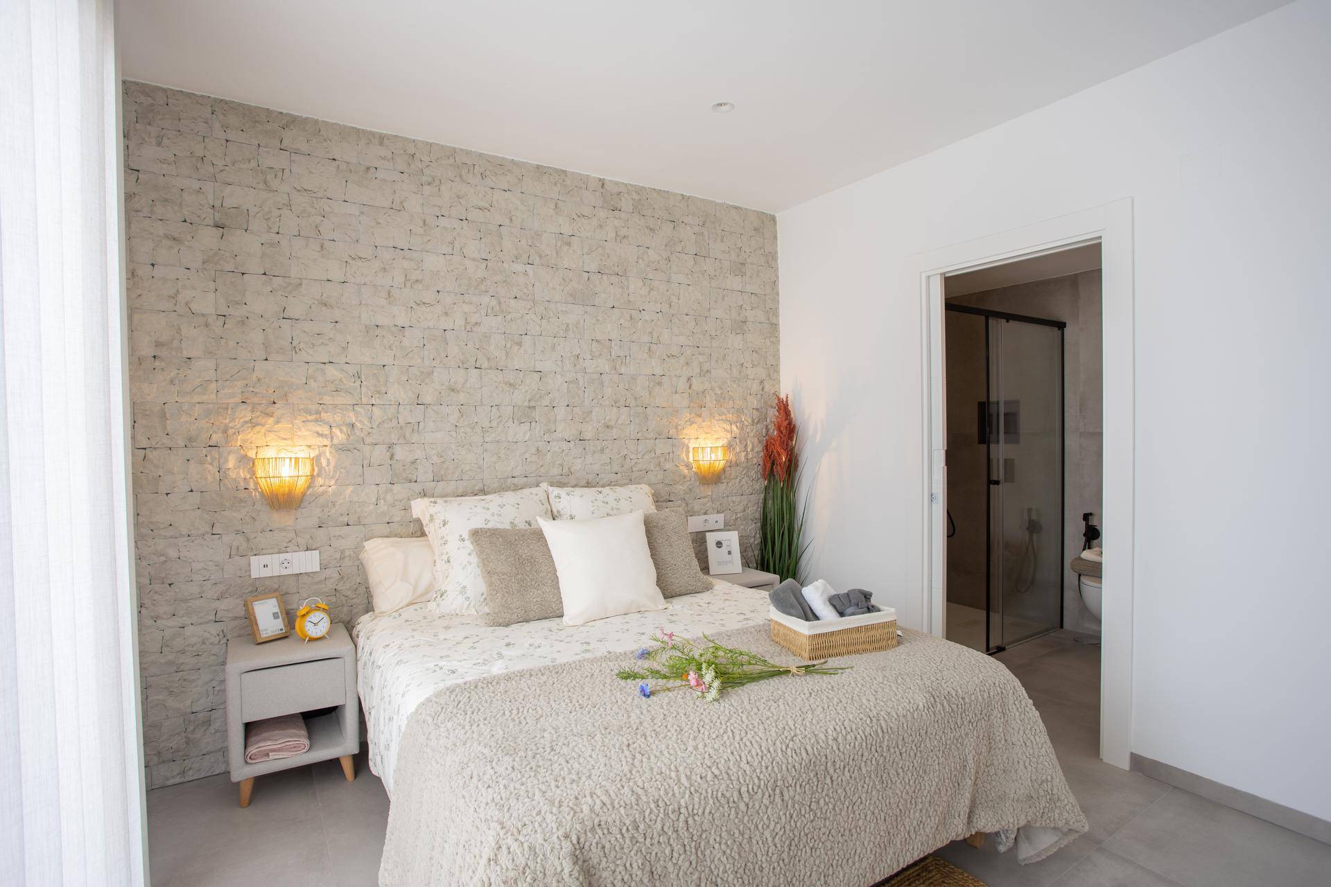 Gemütliches Schlafzimmer mit Steinwand, Doppelbett und direktem Zugang zum Badezimmer.