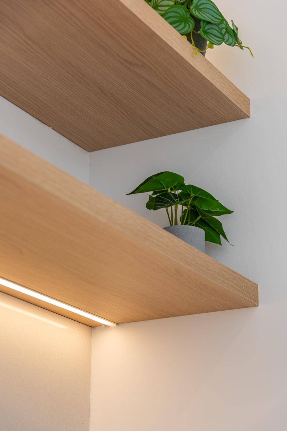 Detailaufnahme von schwebenden Holzregalen mit integrierter Beleuchtung in der Küche.