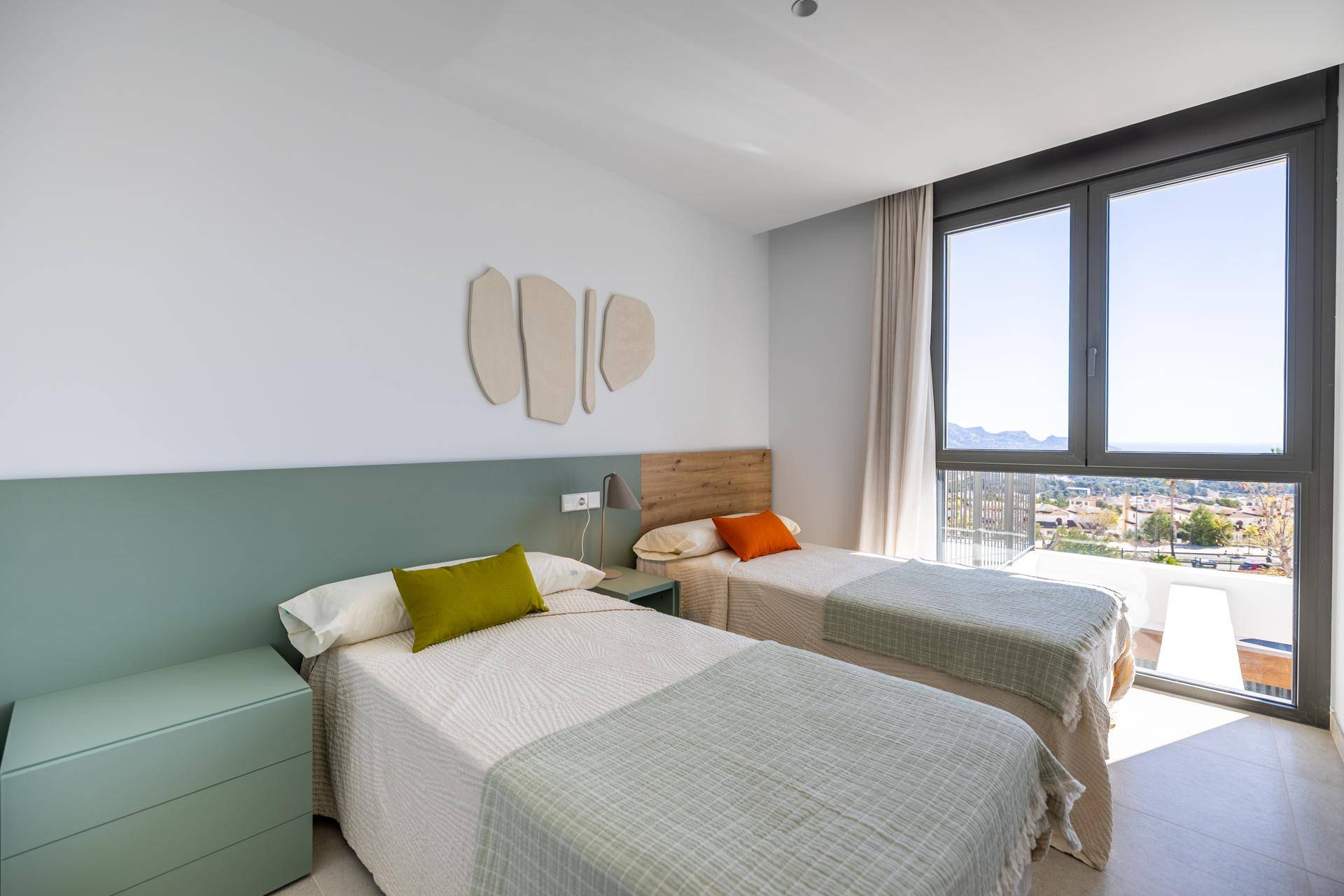 Helles Schlafzimmer mit zwei Einzelbetten, großen Fenstern und Blick auf die Umgebung.
