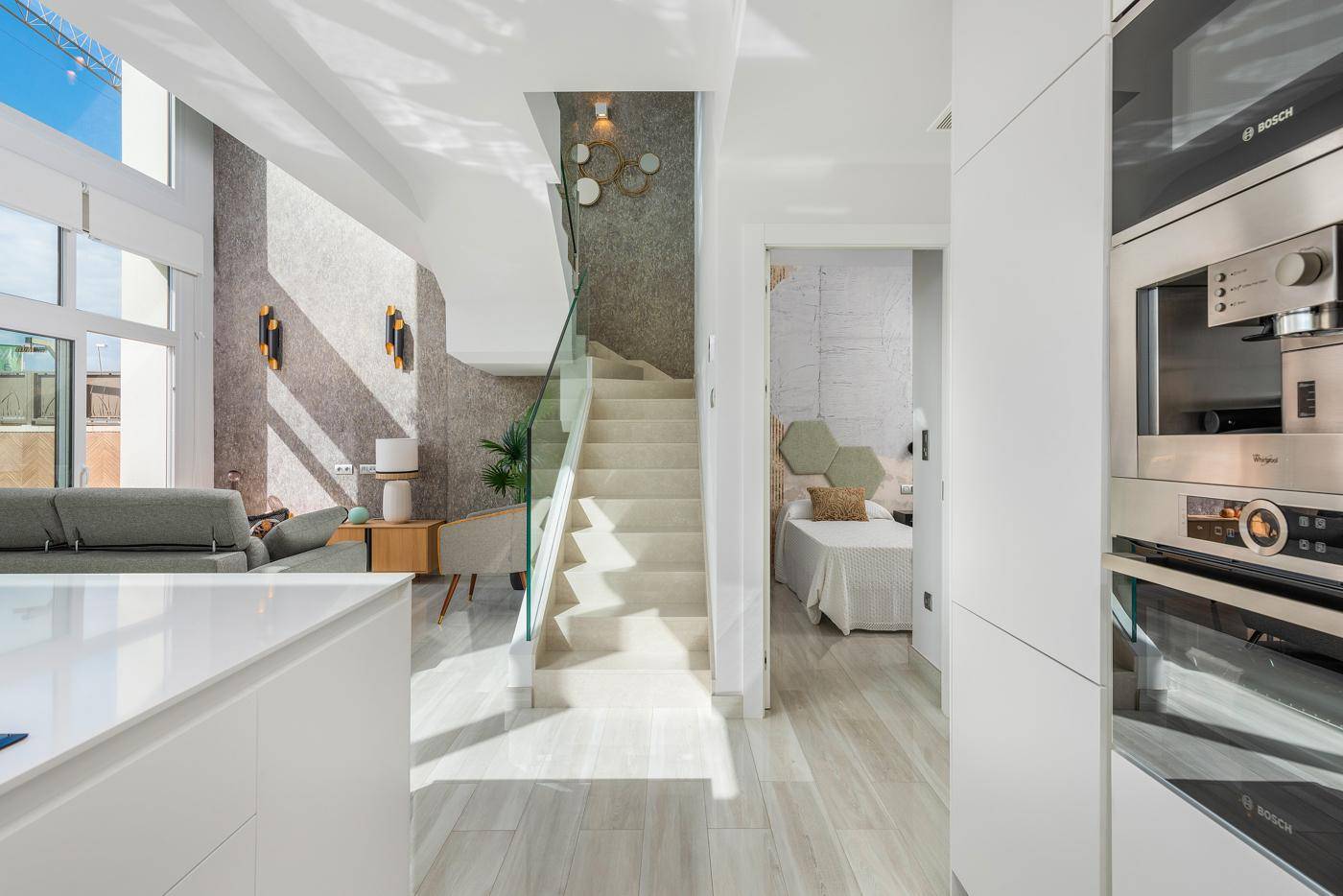 Heller Flur mit Treppe und Blick in ein Schlafzimmer, gekennzeichnet durch moderne Oberflächen und viel Licht.