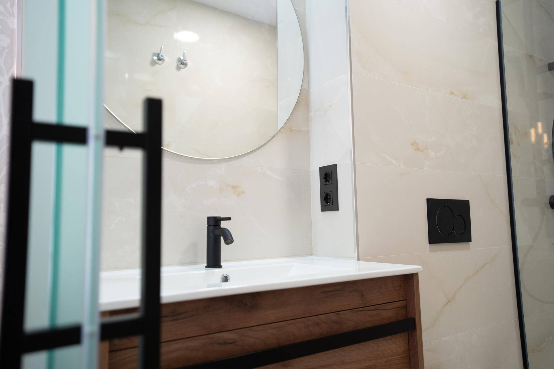 Modernes Badezimmer mit Waschtischunterschrank, rundem Spiegel und schwarzen Armaturen.