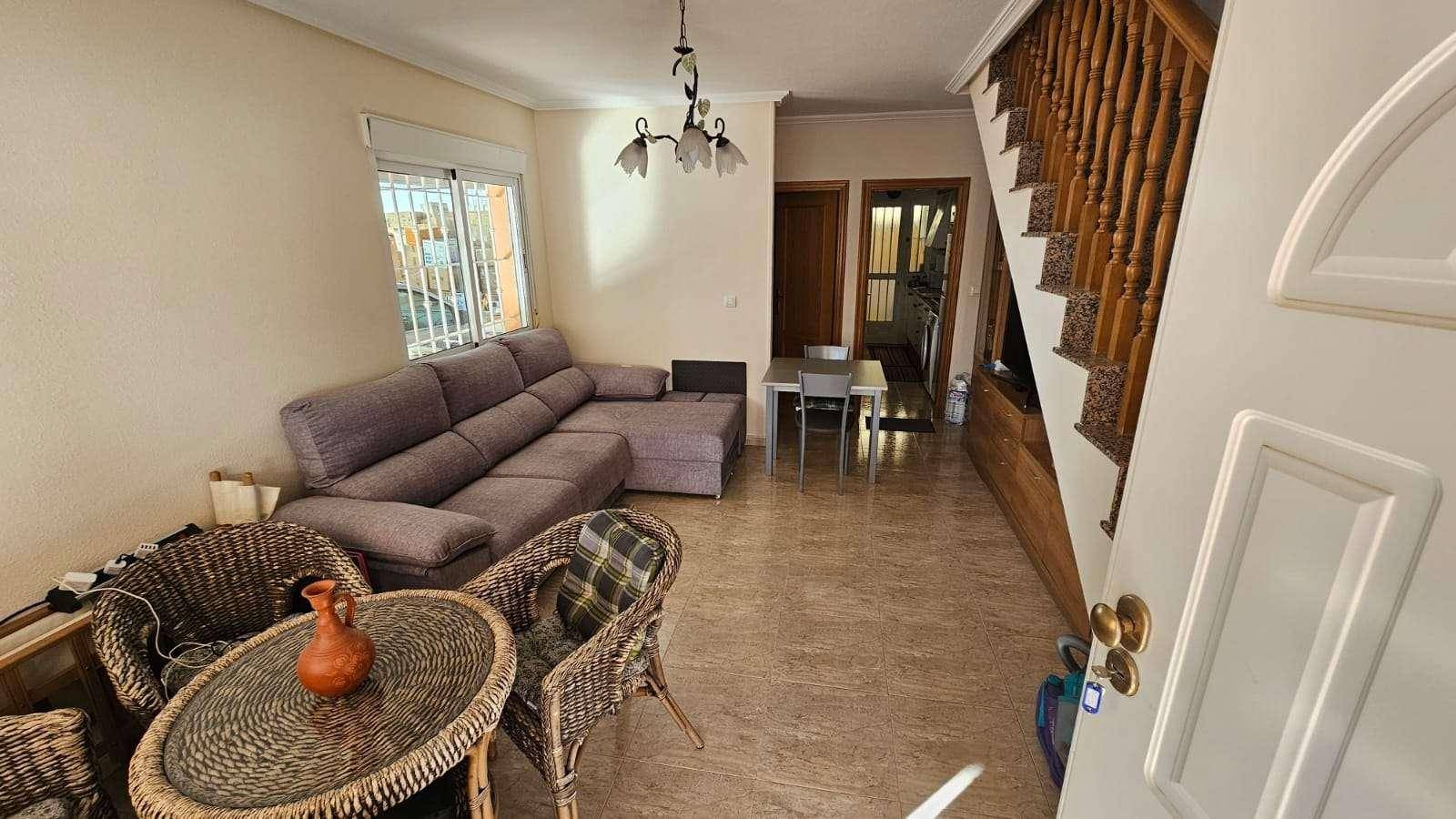 Wohnzimmer mit beigem Fliesenboden, Ecksofa und Holztreppe zum Obergeschoss.