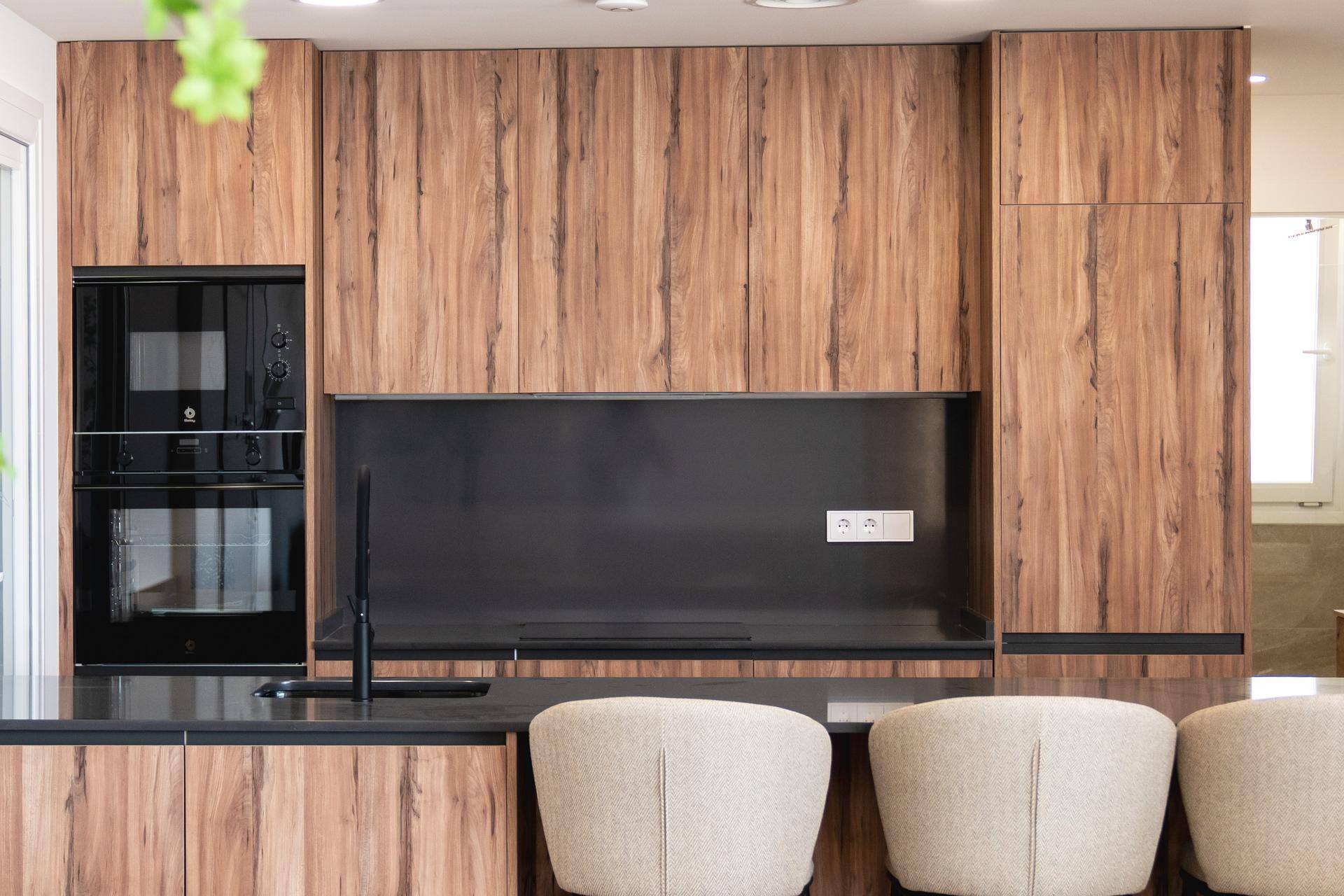 Integrierte Küchengeräte in einer modernen Holzküche mit schwarzer Rückwand und Arbeitsplatte.