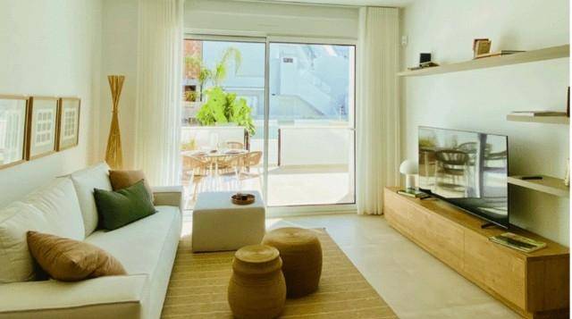 Helles Wohnzimmer mit weißem Sofa, Holzmöbeln und Zugang zu einem Außenbereich.