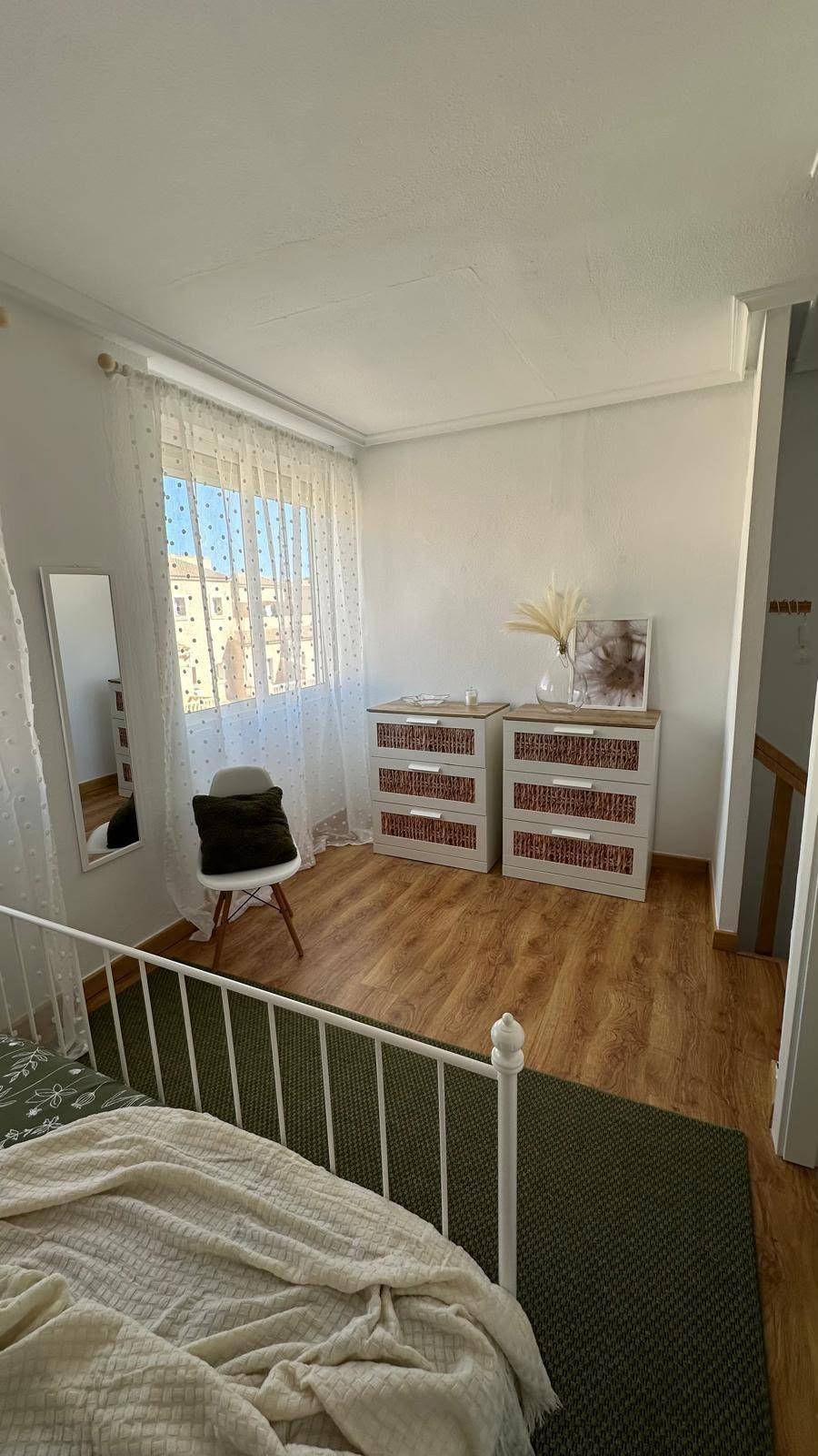 Schlafzimmer mit Holzboden, Nachttischen und einem Spiegel, hell durch Tageslicht.