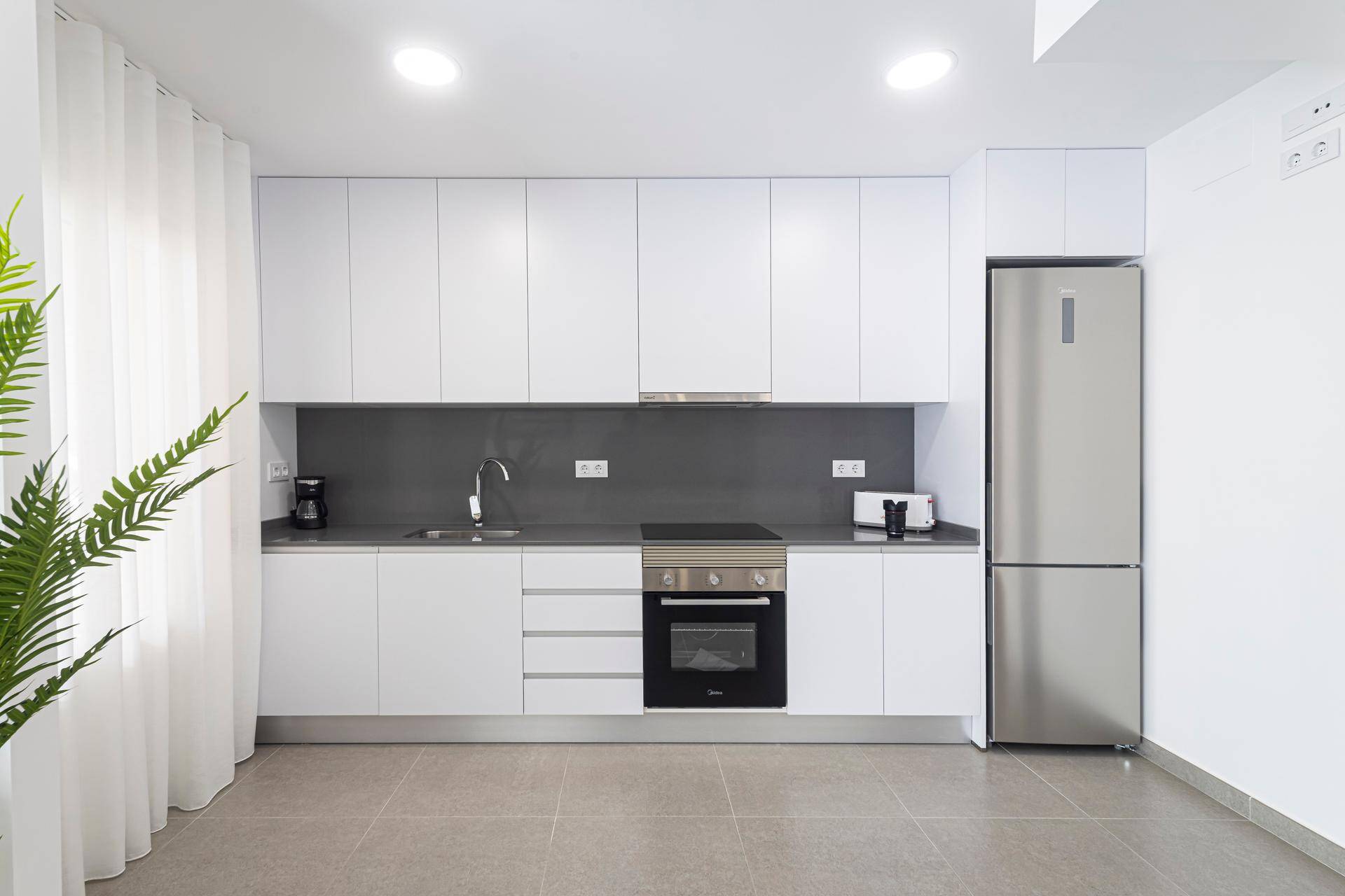 Moderne Einbauküche mit weißen Schränken, dunkler Arbeitsplatte und integrierten Geräten.
