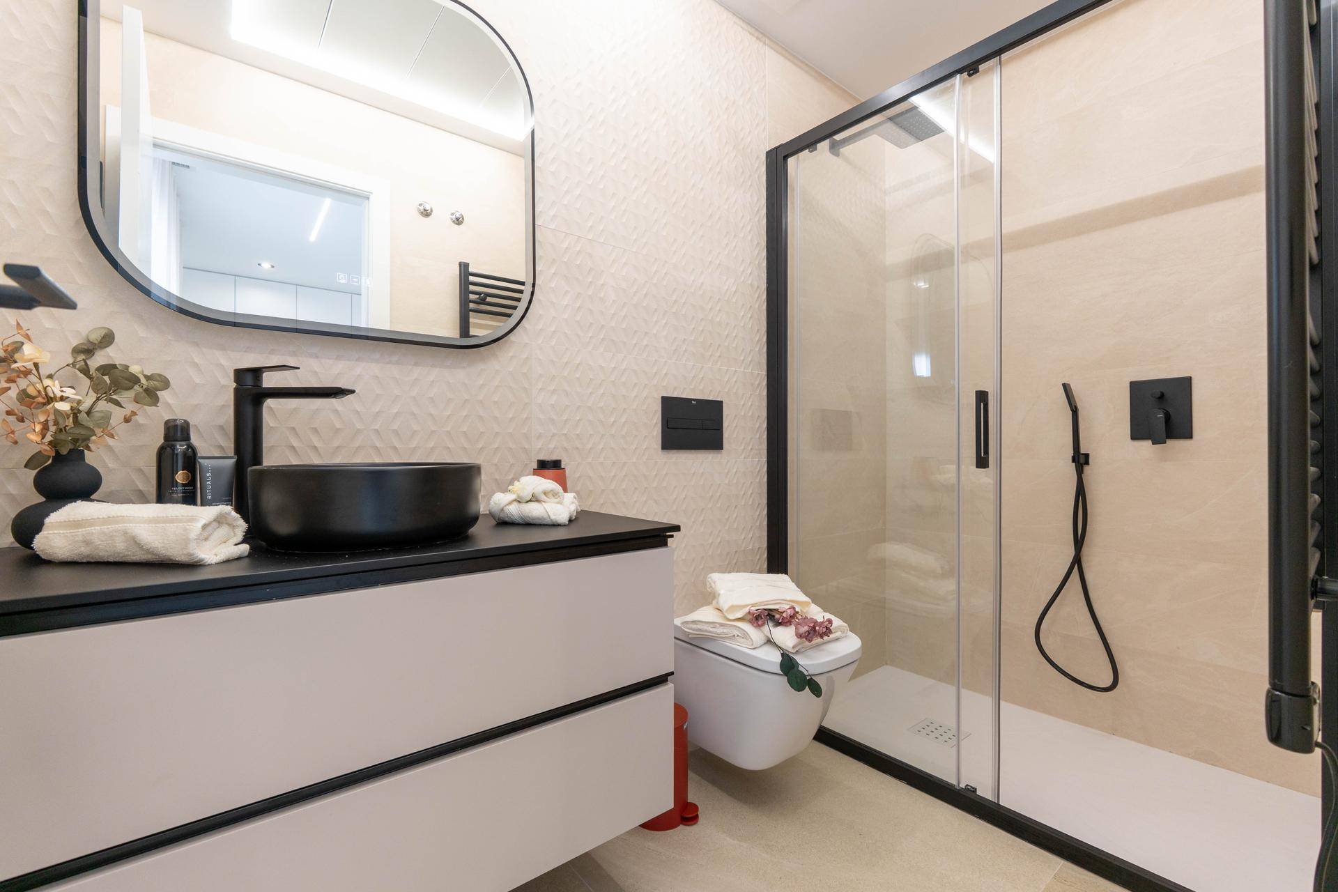 Modernes Badezimmer mit begehbarer Dusche, schwarzem Waschbecken und stilvollen Fliesen.