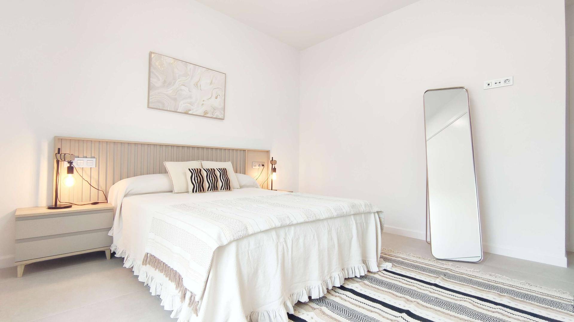 Helles Schlafzimmer mit Doppelbett, Nachttischen und einem großen Spiegel.