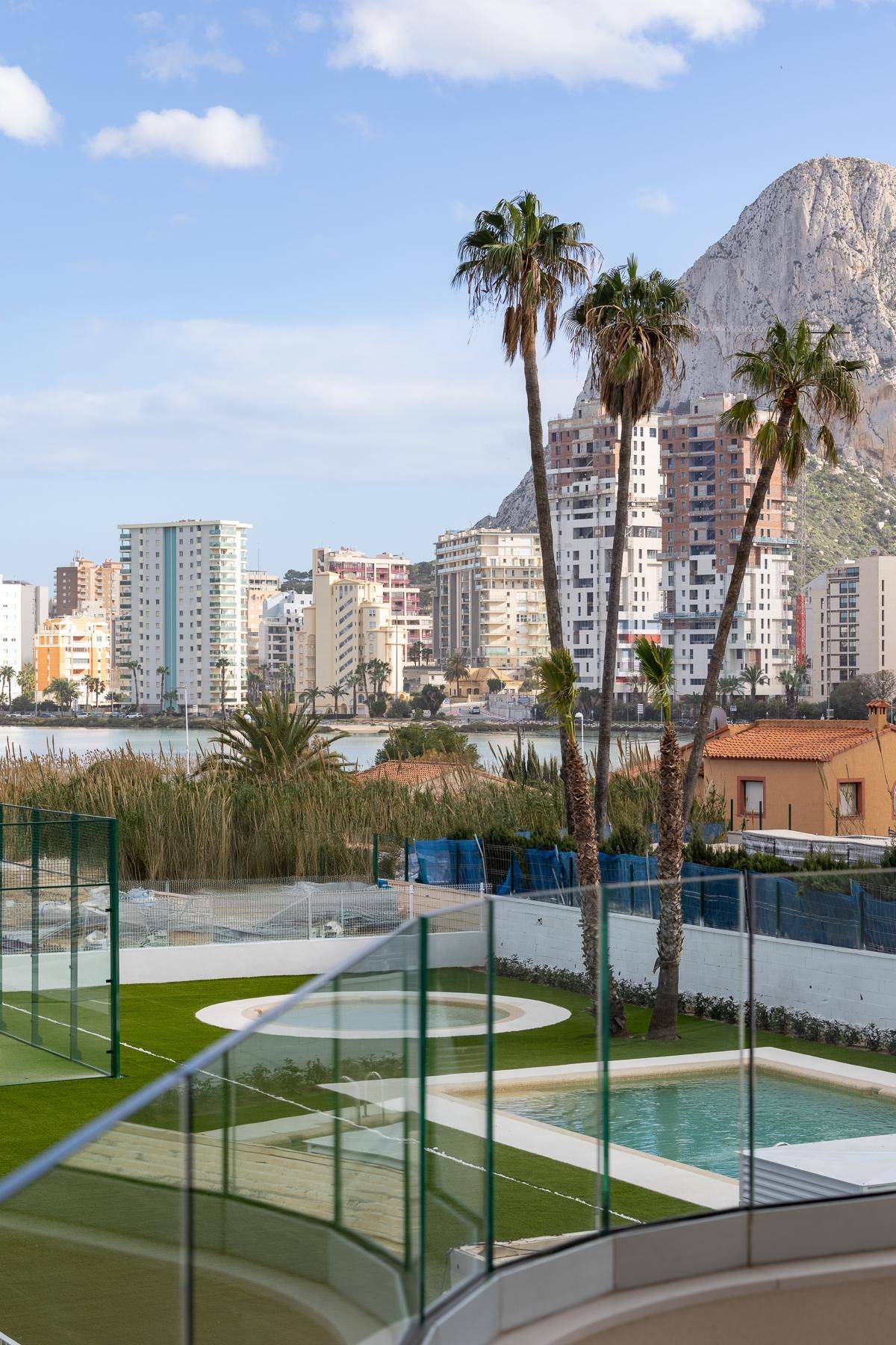 Gepflegter Außenbereich mit Pools, Tennisplatz, Palmen und Bergblick auf die Stadt.