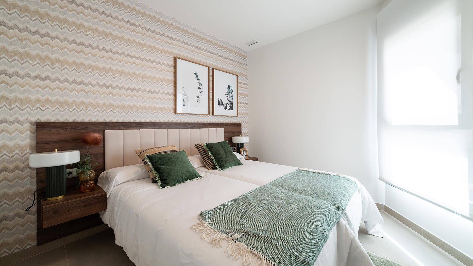 Helles Schlafzimmer mit zwei Einzelbetten, gemusterter Tapete und grünen Akzenten.