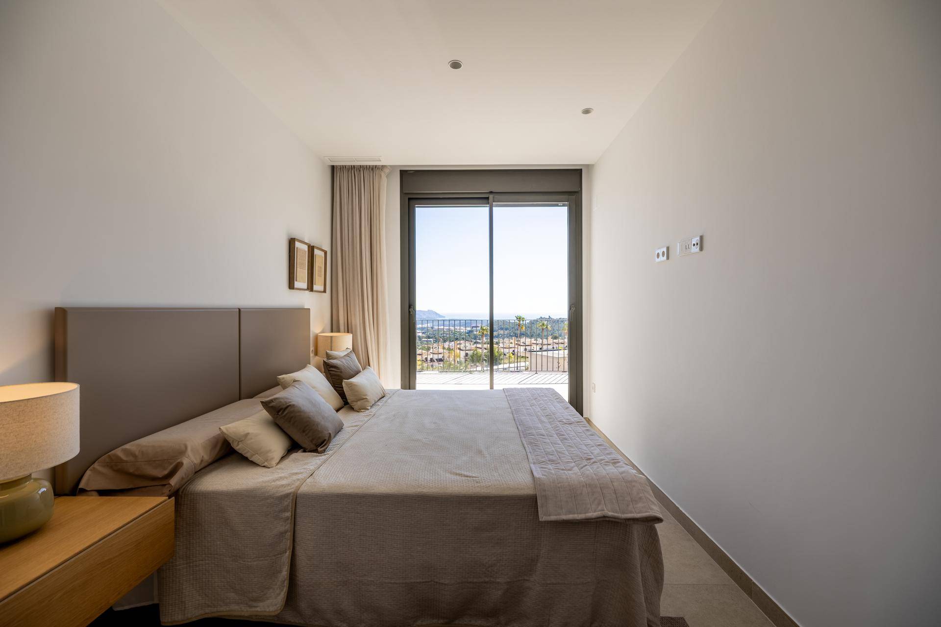 Helles Schlafzimmer mit Doppelbett, großen Schiebetüren und weitem Blick auf die Landschaft.