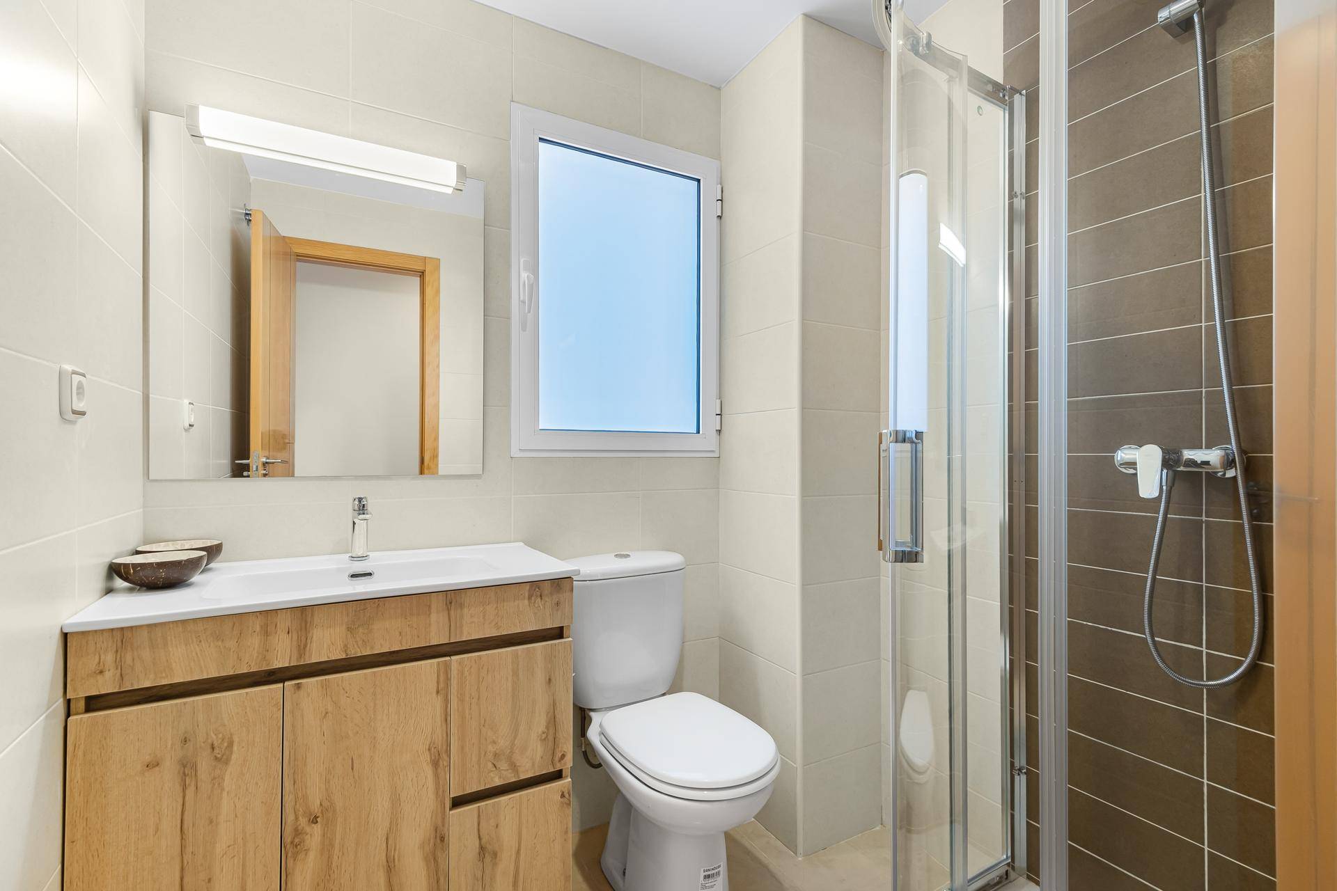Modernes Badezimmer mit Duschkabine, WC, Holzwaschtisch und Fenster für Belüftung.