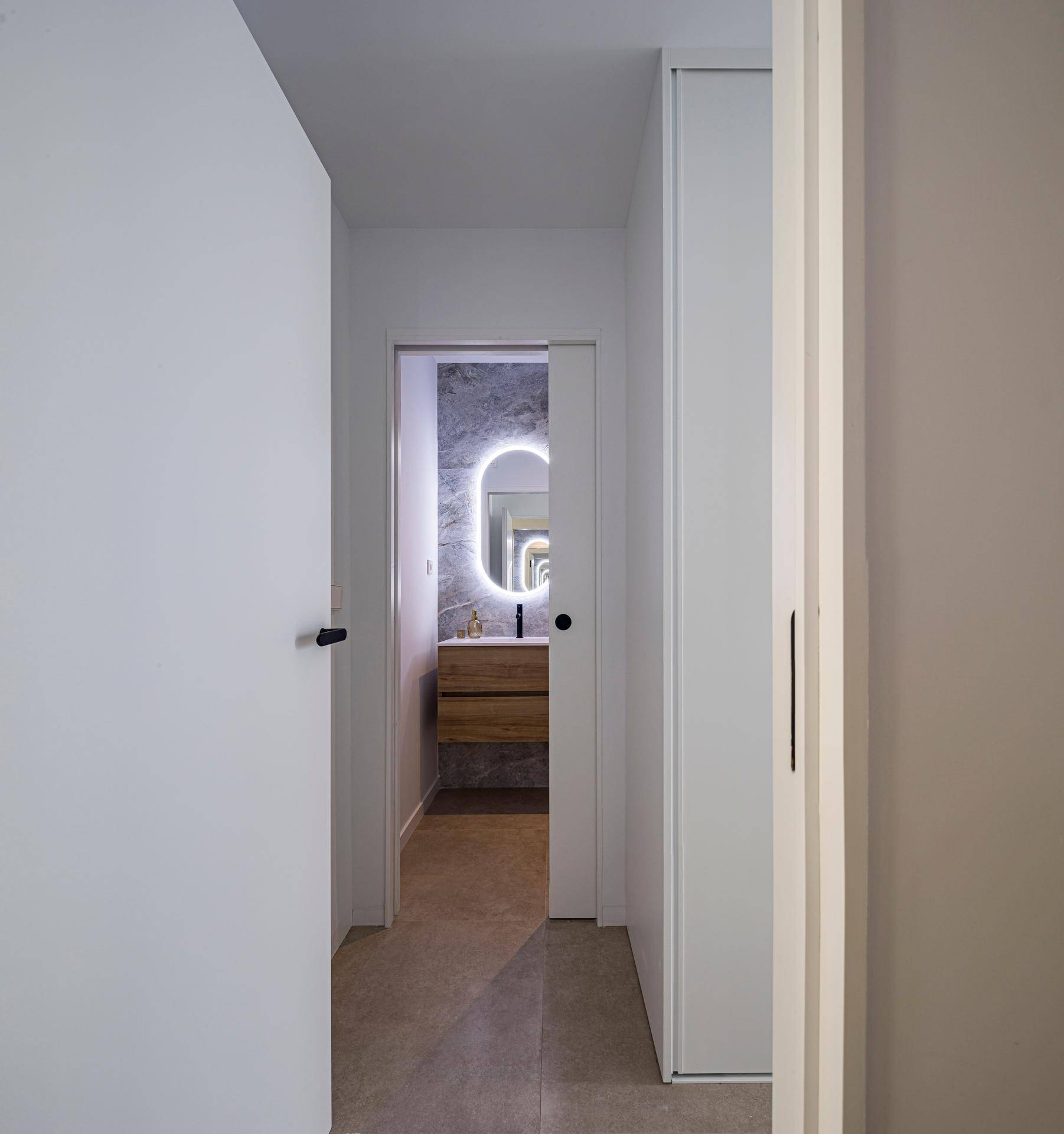 Heller Flur mit Blick auf ein modernes Badezimmer mit beleuchtetem Spiegel.
