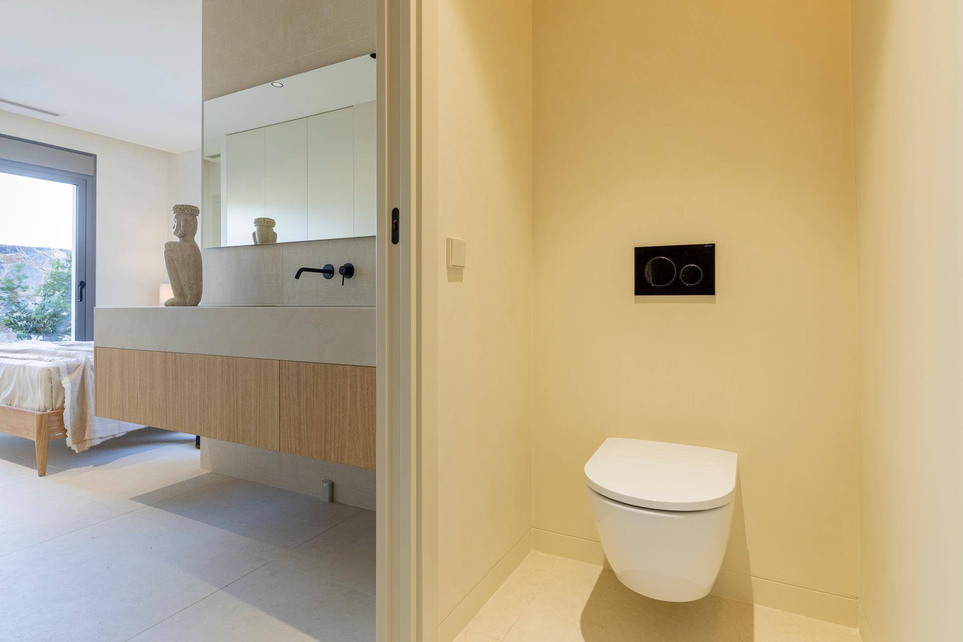 Modernes WC mit wandhängender Toilette und Blick in den angrenzenden Schlafbereich.