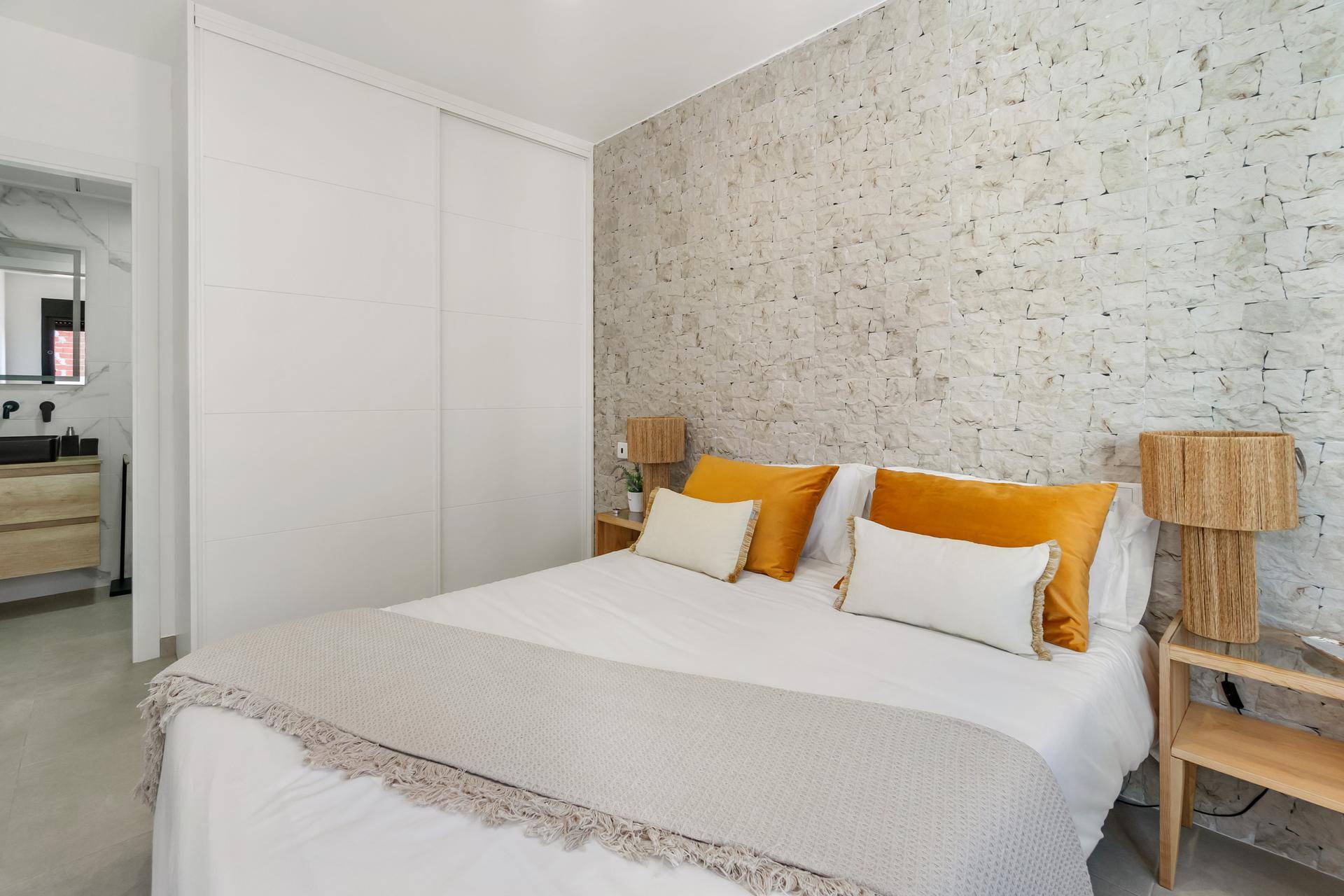 Schlafzimmer mit integriertem weißen Kleiderschrank, Steinwand und Doppelbett.