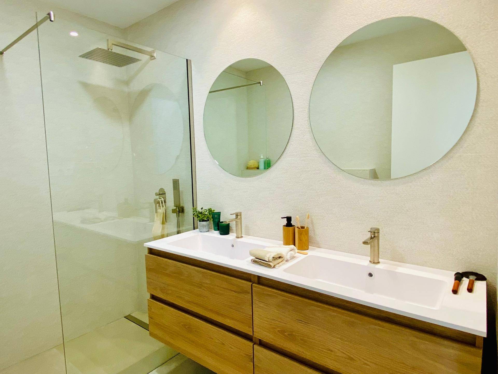 Modernes Badezimmer mit Doppelwaschbecken, zwei runden Spiegeln und einer geräumigen begehbaren Dusche.