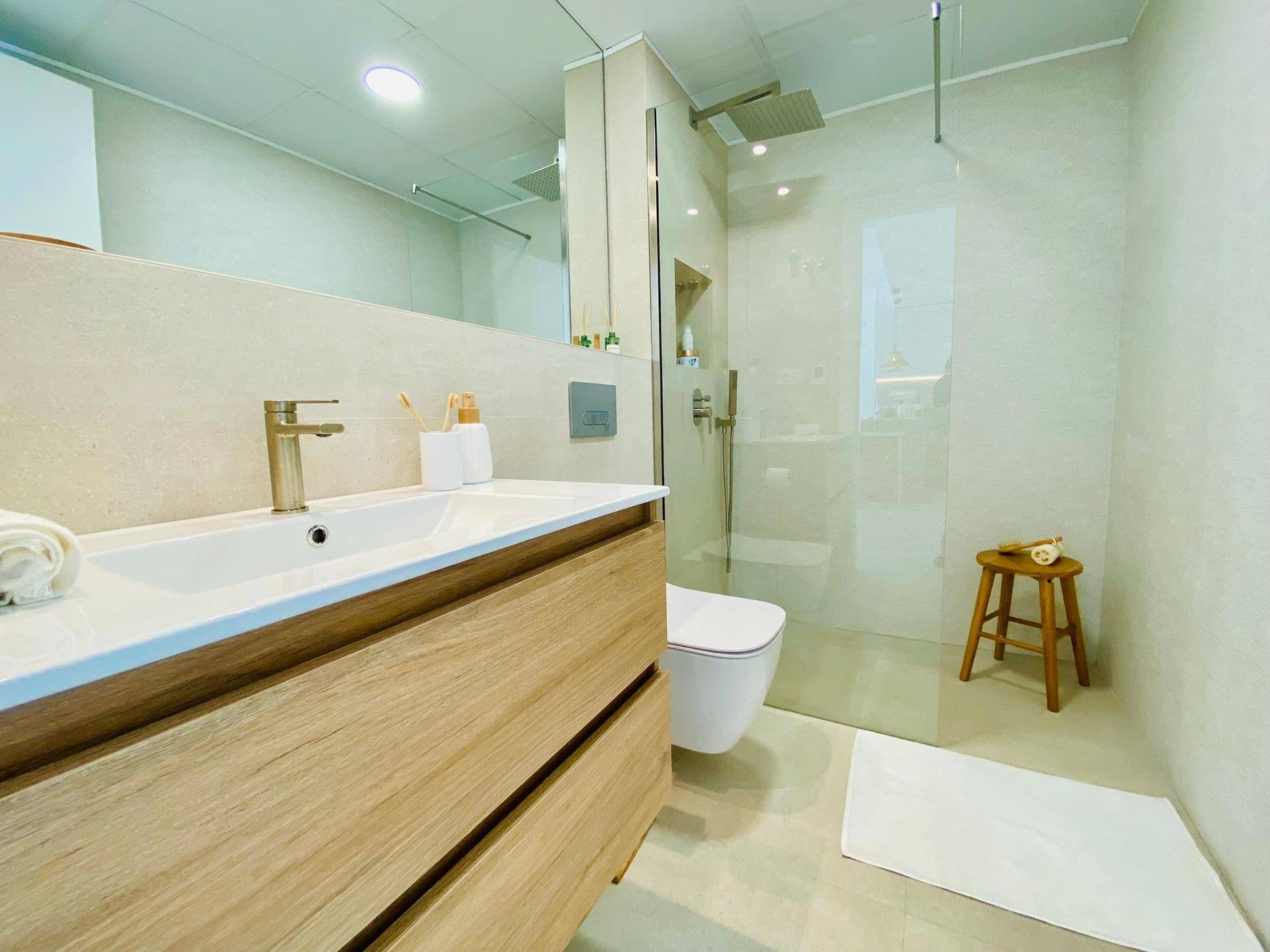 Helles Badezimmer mit modernem Waschtisch, wandhängendem WC und großer begehbarer Regendusche.