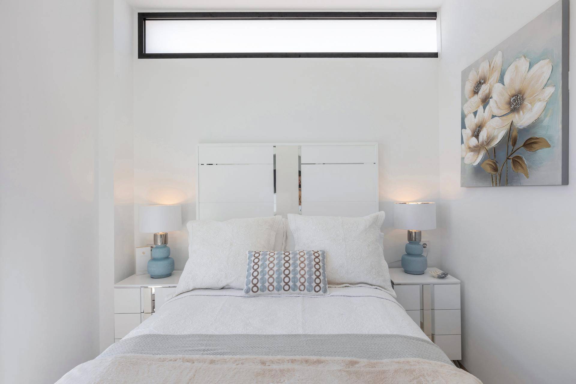 Helles Schlafzimmer mit Doppelbett, Nachttischen und schmalem Oberlichtfenster.