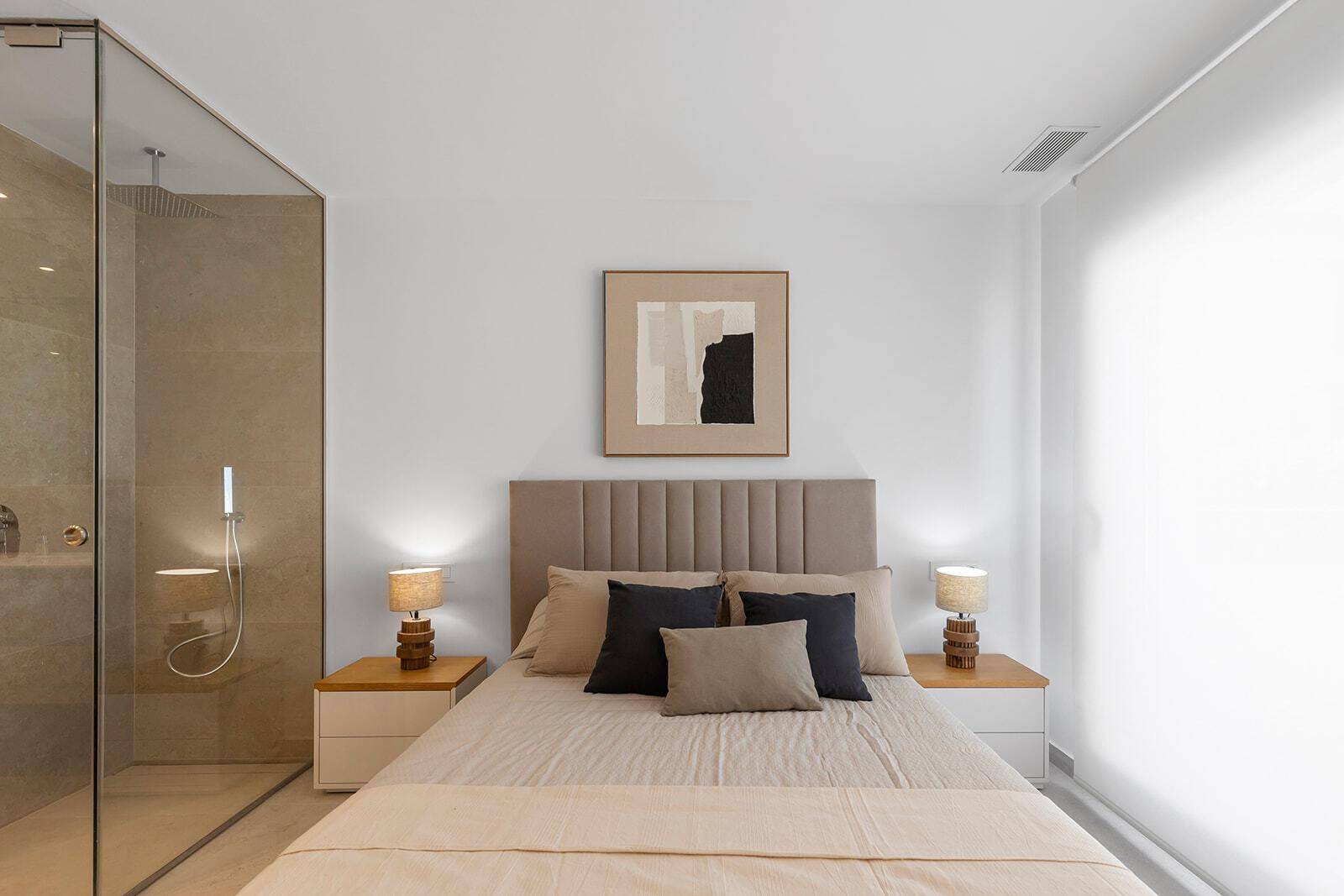 Helles Schlafzimmer mit großem Bett, Nachttischen und indirekter Beleuchtung, offen zum Badbereich.