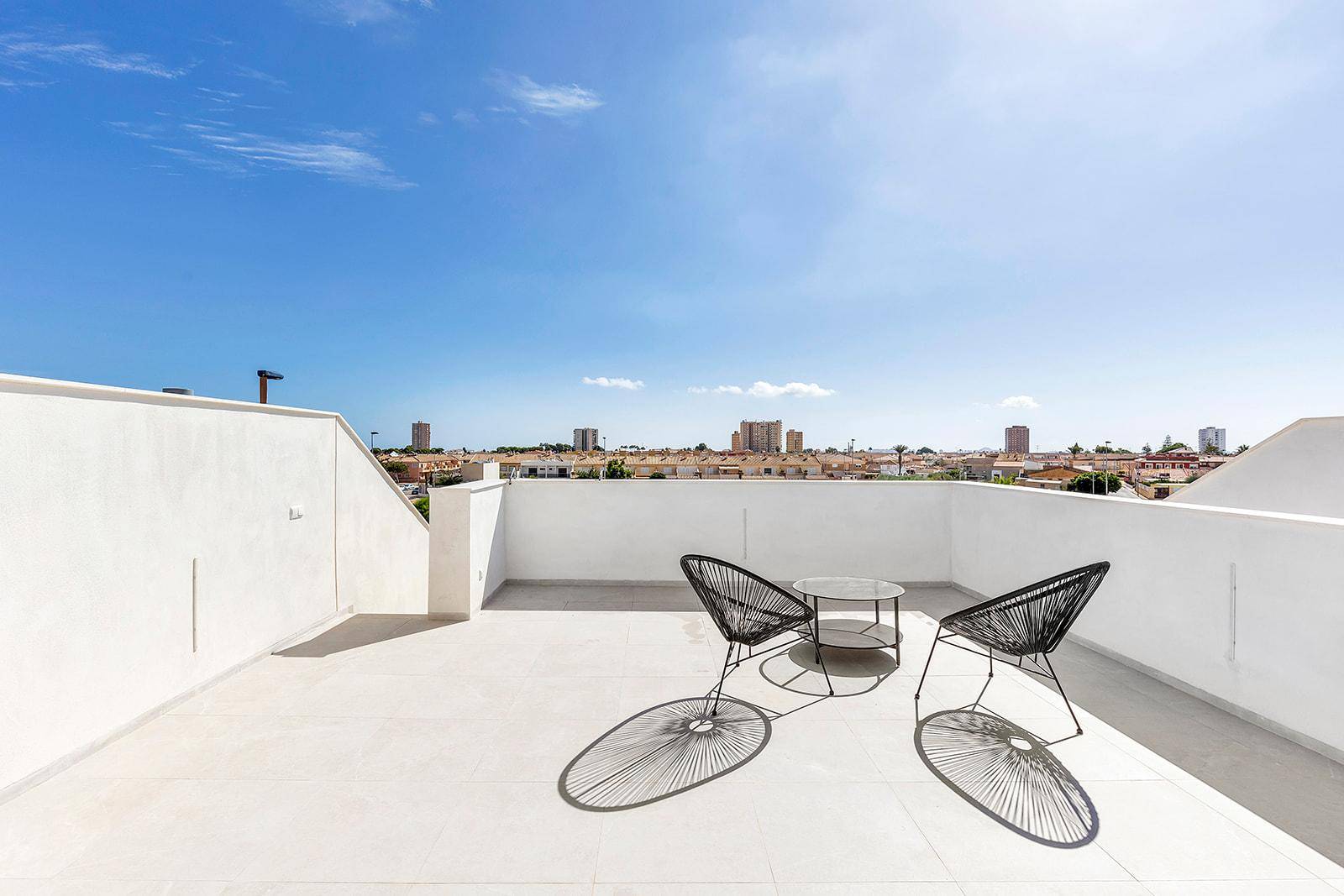 Minimalistisch eingerichtete Dachterrasse mit Stadtblick unter blauem Himmel.