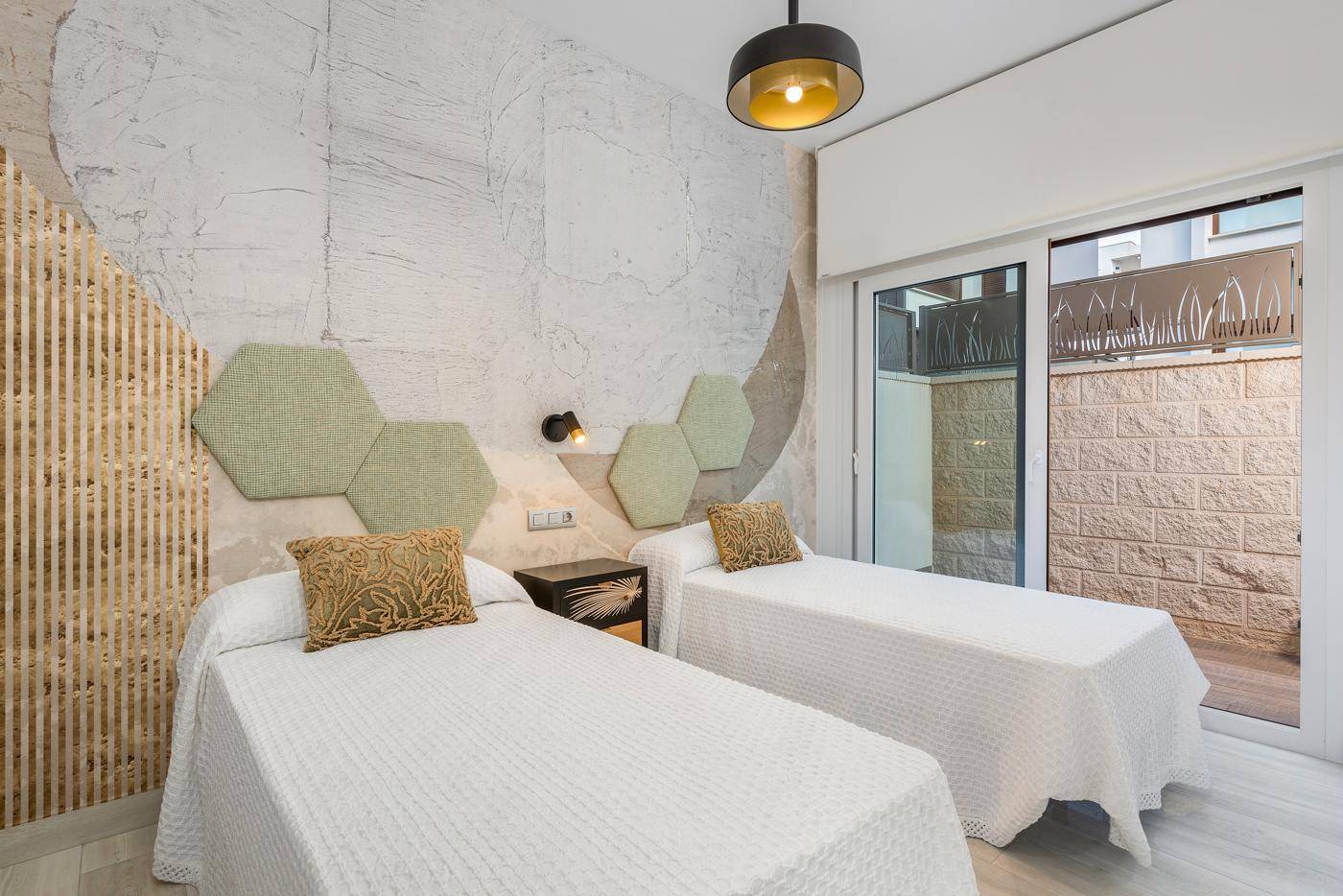 Schlafzimmer mit zwei Einzelbetten, dekorativer Wandgestaltung und Zugang zu einem kleinen Außenbereich.